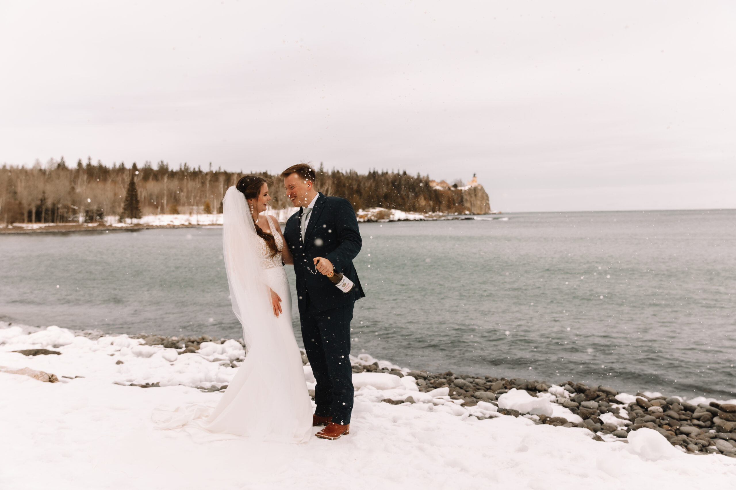 Elopement couple doing a champagne spray at silver bay beach, Minnesota with Splitrock lighthouse in the background