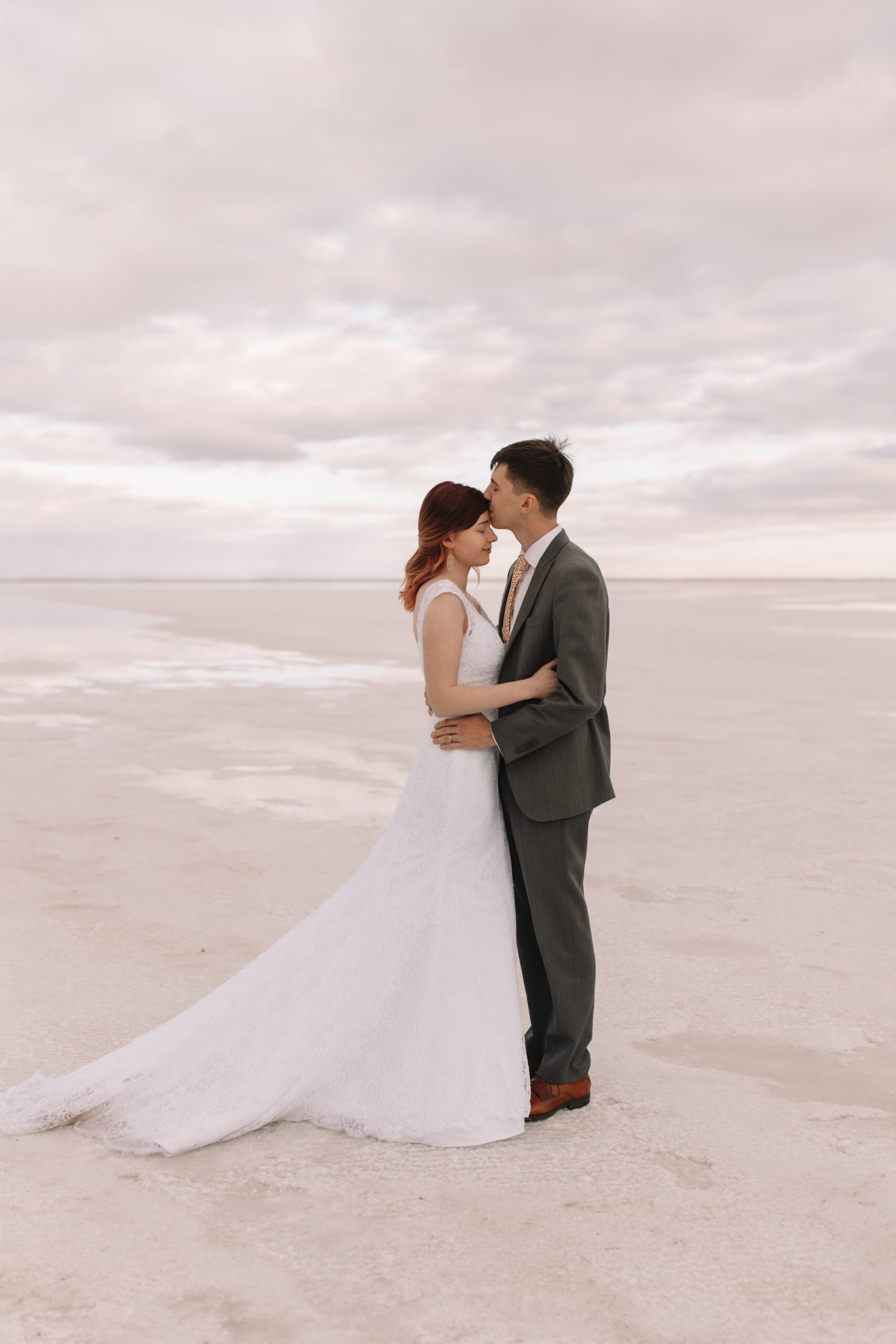 Elopement couple holding each other while the groom kisses his brides forehead on the white salt flats in Utah