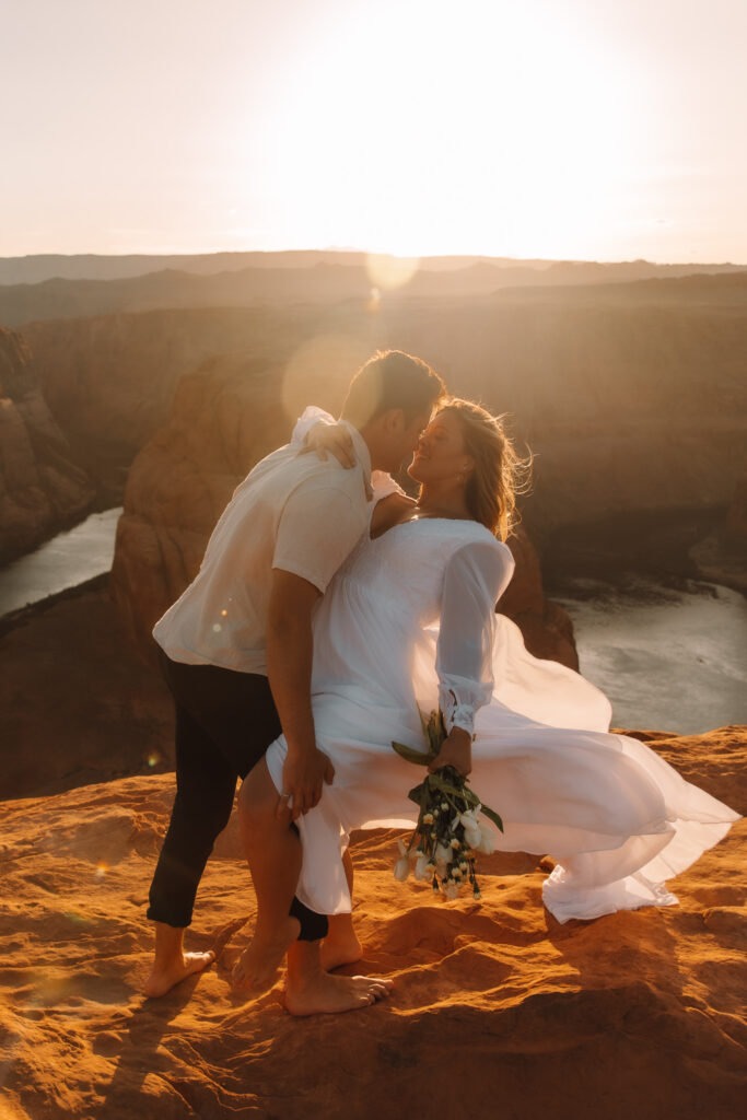 Groom leaning his bride back nose touching as the sun sets behind them at Horse shoe bend in Arizona