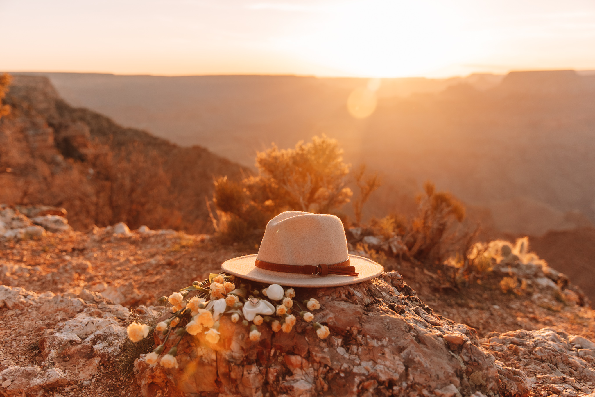 Stunning detail photo of a hat lying next to a bouquet of yellow and white flowers on top of a rock in the Grand Canyon