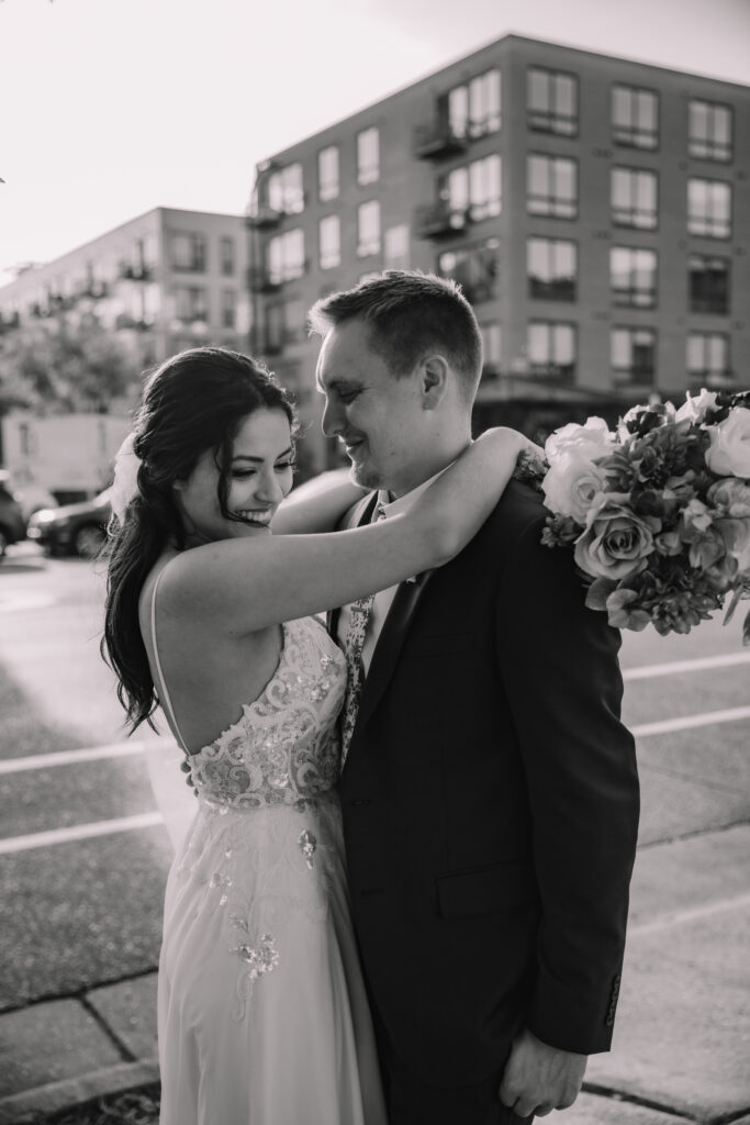 Black and White photo of a Bride standing with her arms around her Groom on the side walk in the City