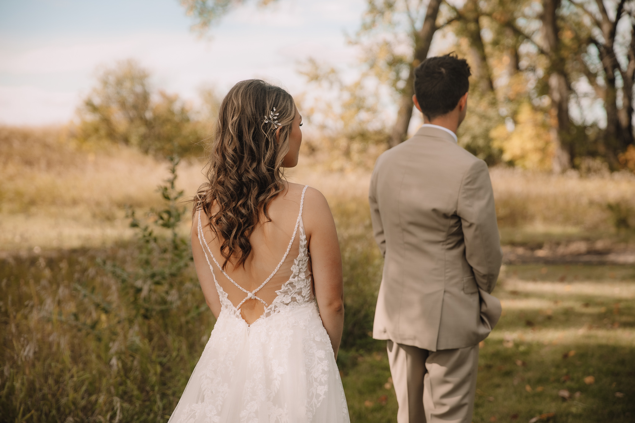 Bride with a beautiful open back dress, standing behind her groom as she gets ready to show him what she looks like for the first time