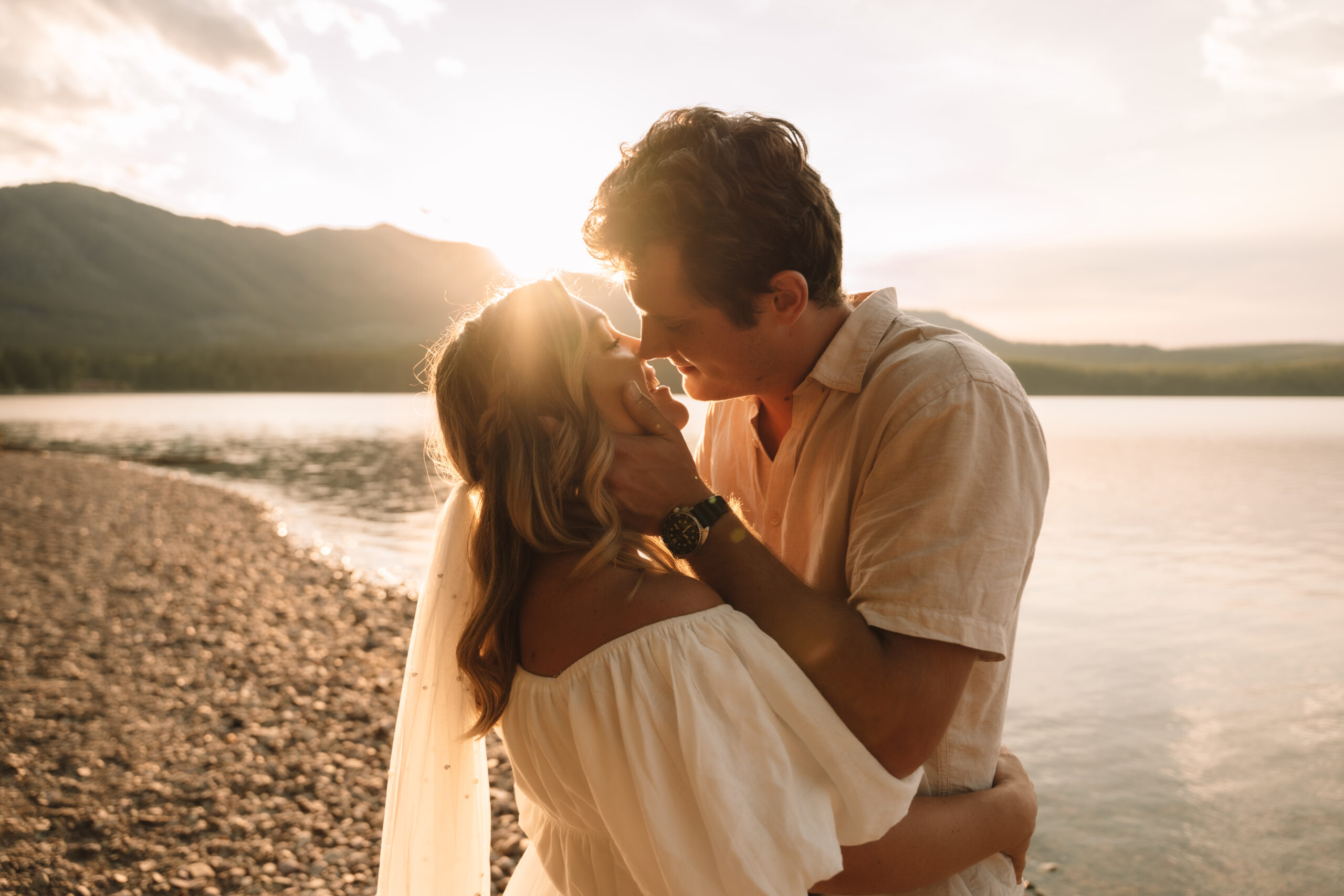 Groom holding bride's face tenderly while staring at her as the sun sets behind them in Glacier National Park