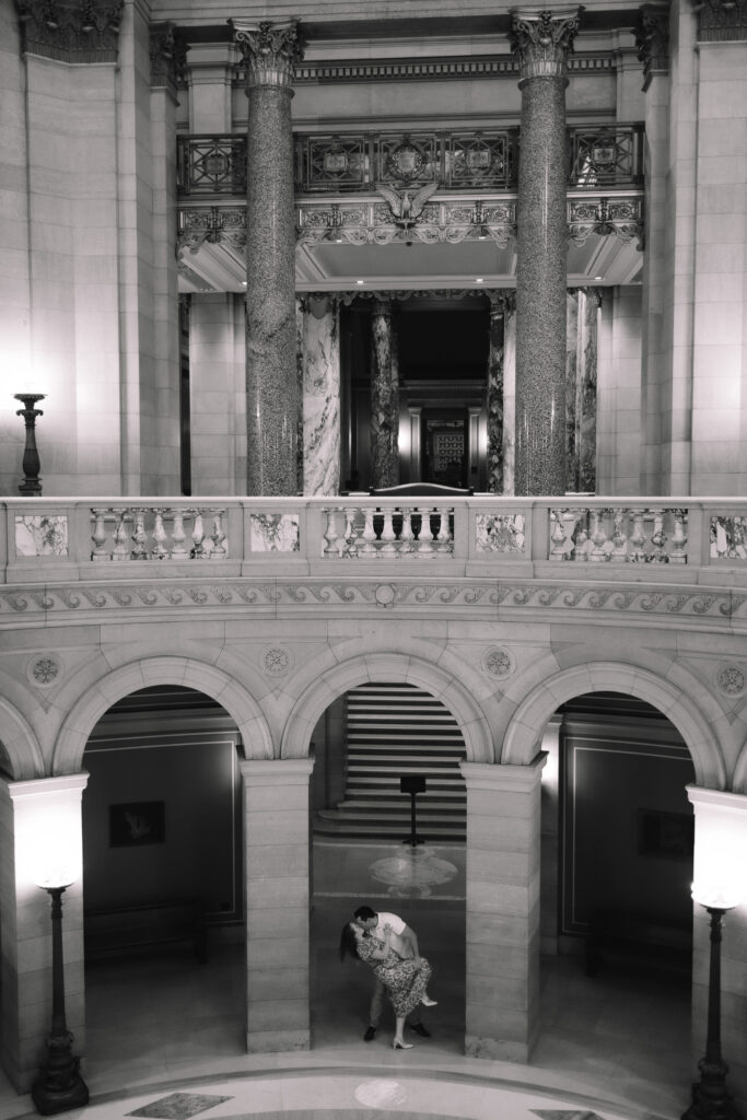 The stunning interior design of the Minnesota State Capitol building and an engagement couple dip kissing in the distance in the middle of the 3 arches