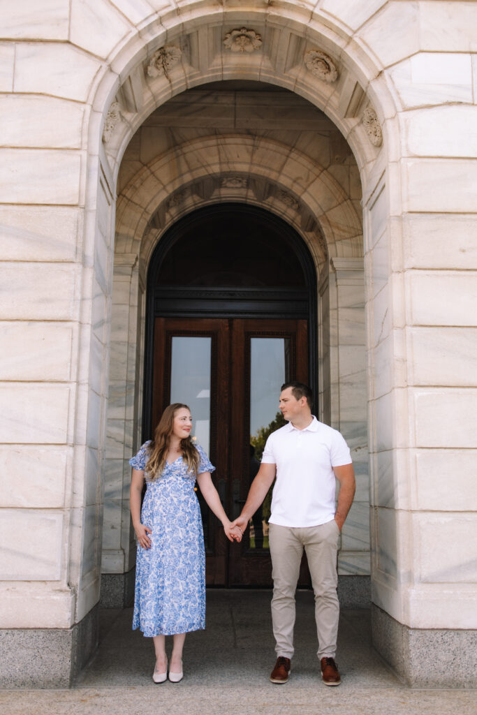 Engagement couple standing side by side, holding hands in front of the Minnesota State Capitol