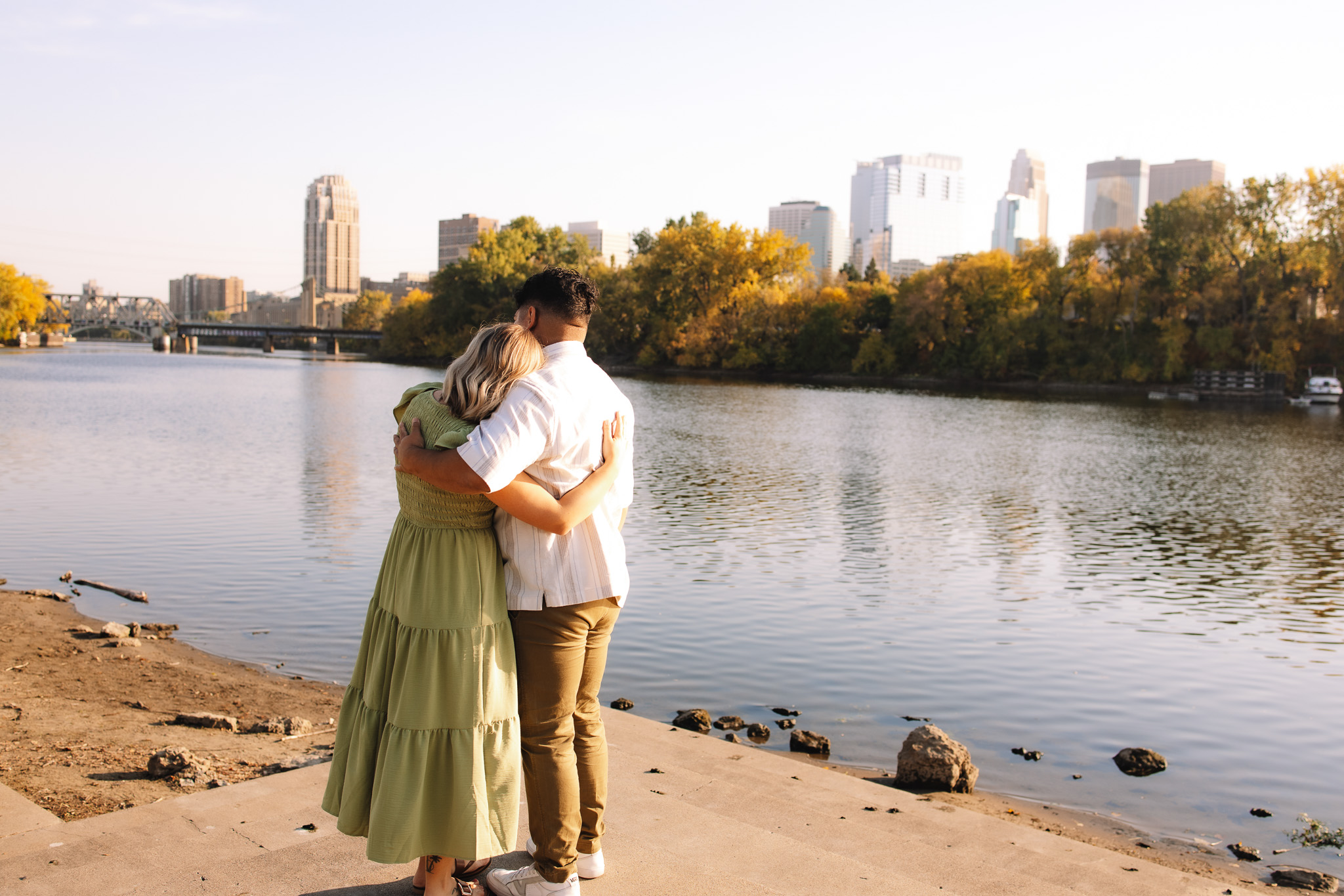 Guy and girl holding each other during their engagement session overlooking the Minneapolis skyline at Boom Island Park