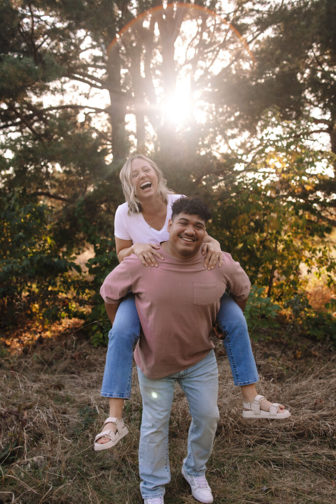 Guy giving girl a piggy back ride during golden hour at Boom Island Park in Minneapolis for their engagement photos