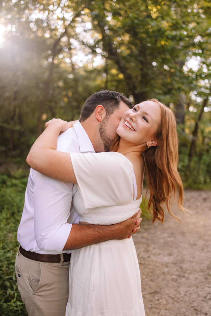 Guy kissing his girl's neck while she laughs looking into the sun at Minihaha Falls - One of the best engagement photo locations in Minneapolis