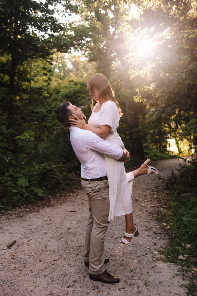 Guy lifting his girl up as the sun shines beautifully behind them