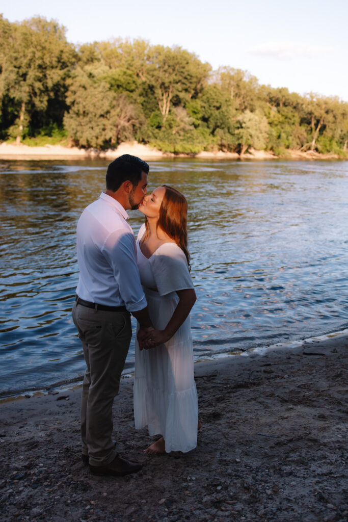 Guy and girl kissing standing in front of a river at Minihah Falls in Minneapolis- One of the best engagement photo locations in Minneapolis