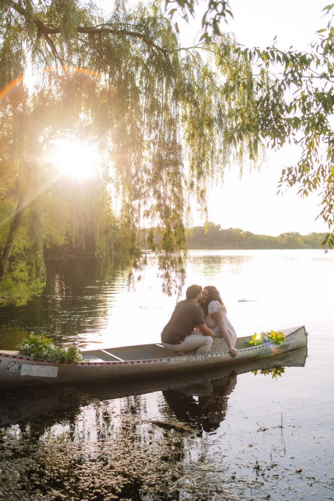 An engagement couple sitting in a canoe kissing during a beautiful sunset at Lake of the isles- One of the best engagement photo locations in Minneapolis