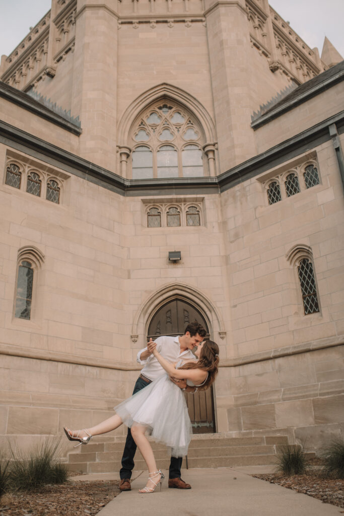 An engagement couple dip kissing in front of a beautiful church building in Minneapolis