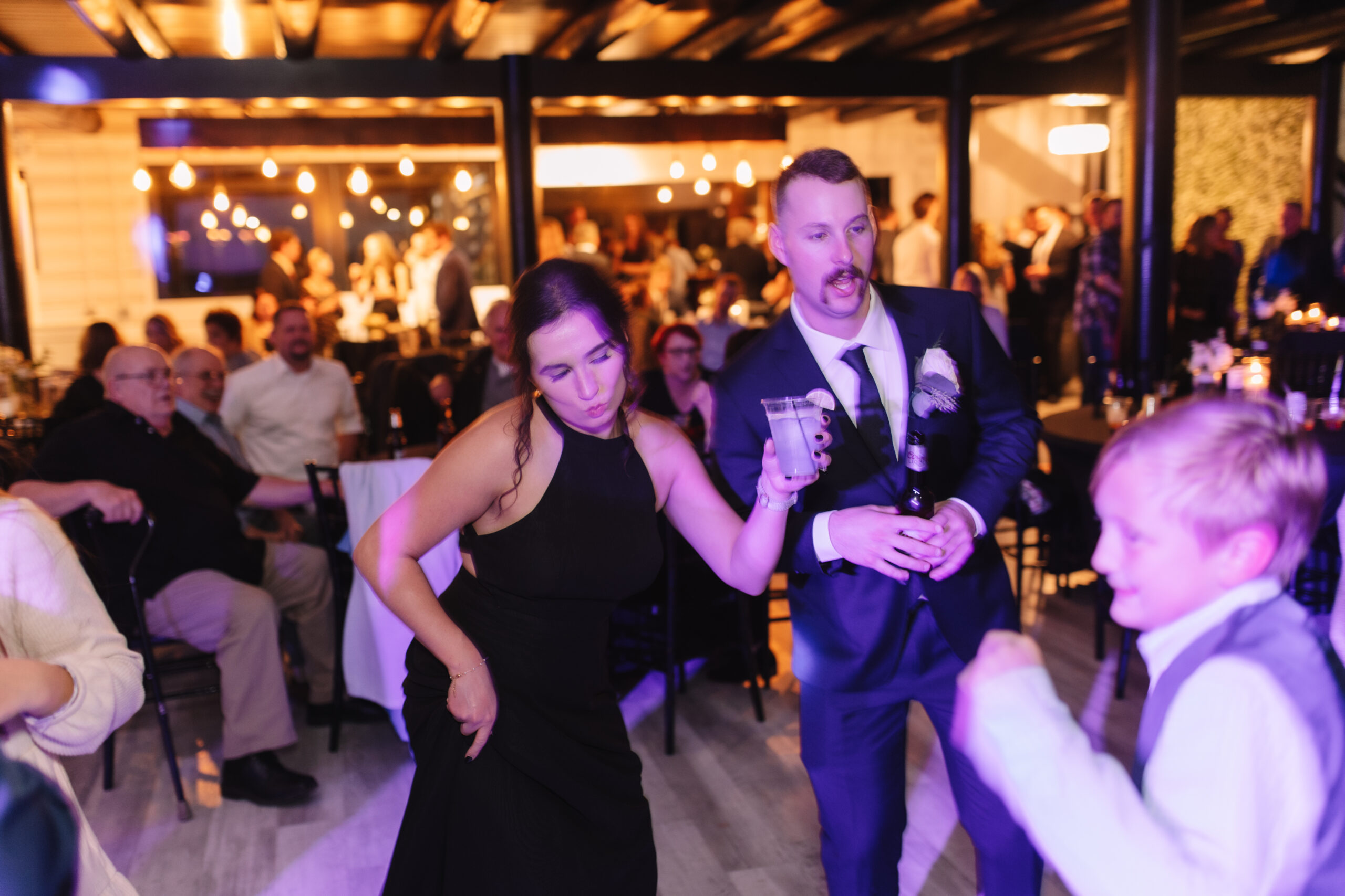 Guests dancing have a fun time on the dance floor at a wedding. Purple and yellow lights surround them