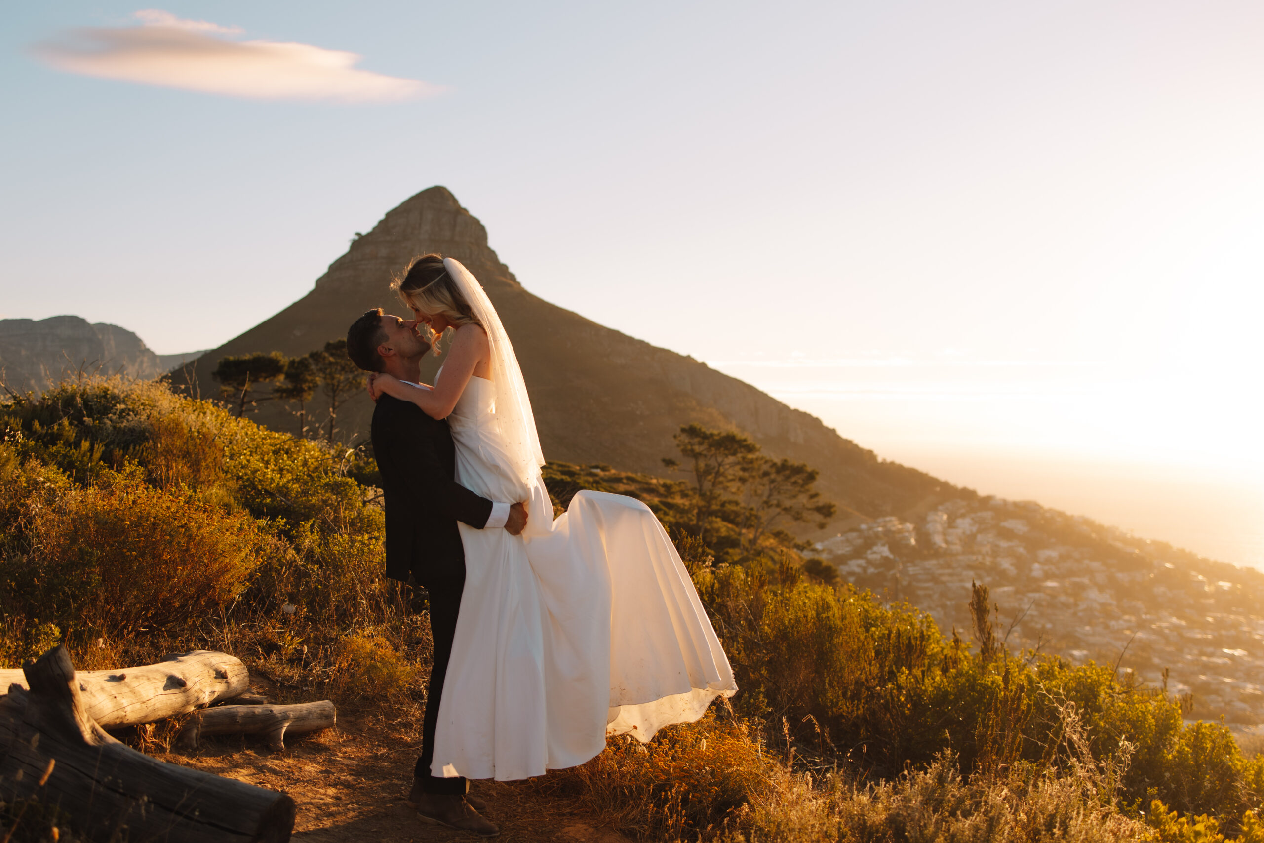 Groom picking up bride while they kiss on top of Signal Hill in Cape Town. Lion's Head is visible in the back ground.