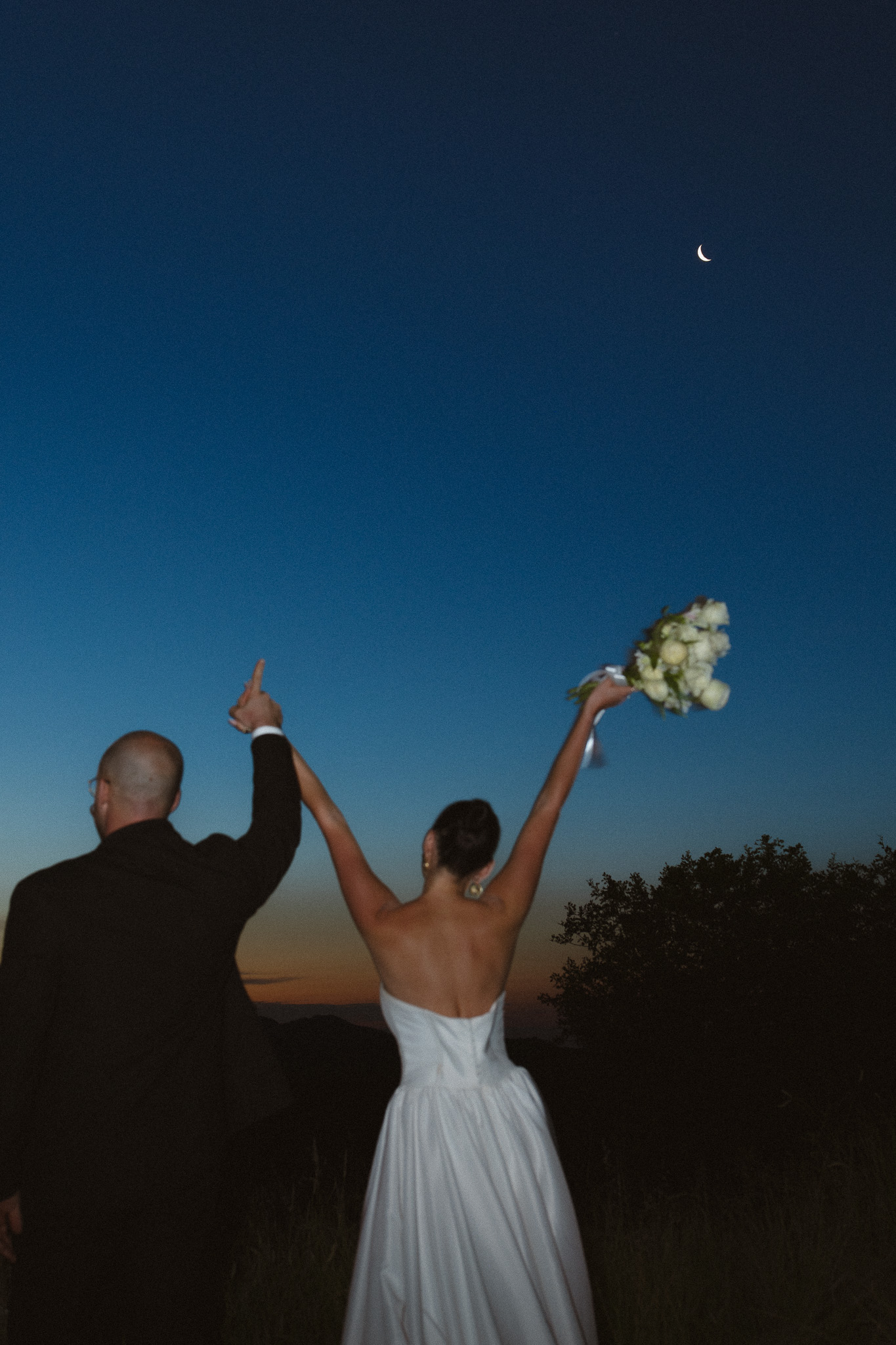 Newlyweds celebrating beneath a crescent moon after their safari elopement