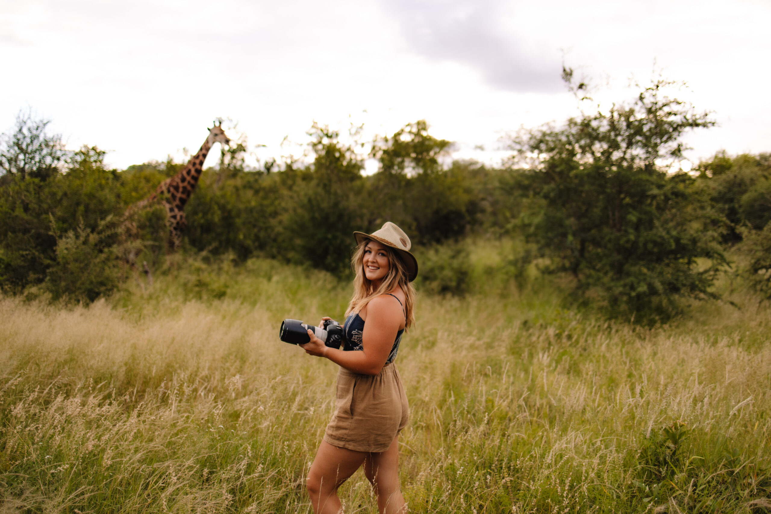South Africa safari elopement photographer Heidi Straus holding her camera with a giraffe behind her