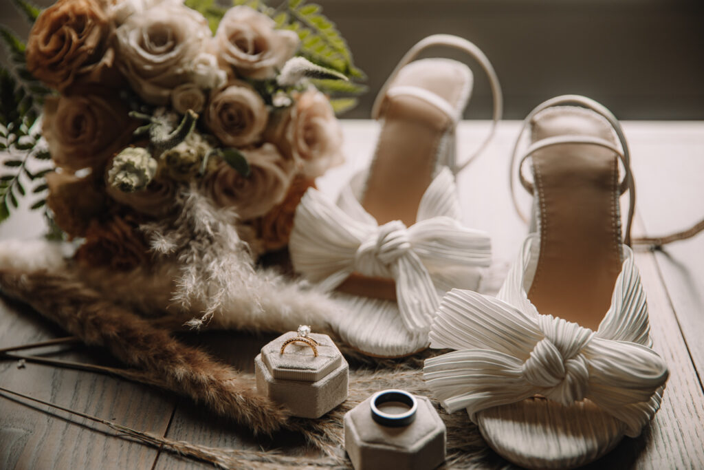 Beautiful wedding flat-lay details of white wedding shoes with bow, rings and boho boquet
