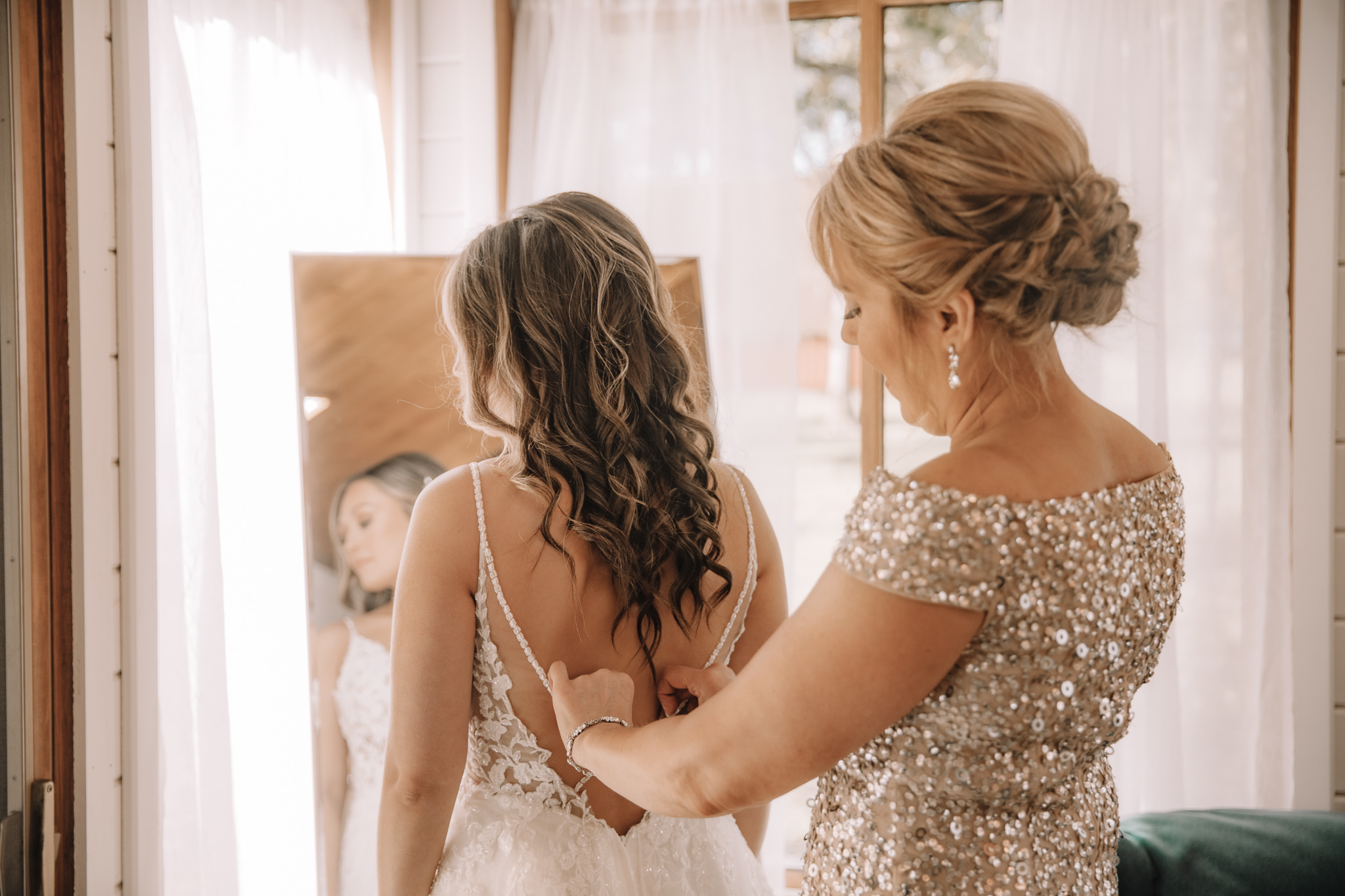 Mother-of-the-bride helping Bride zip up her beautiful open back wedding dress