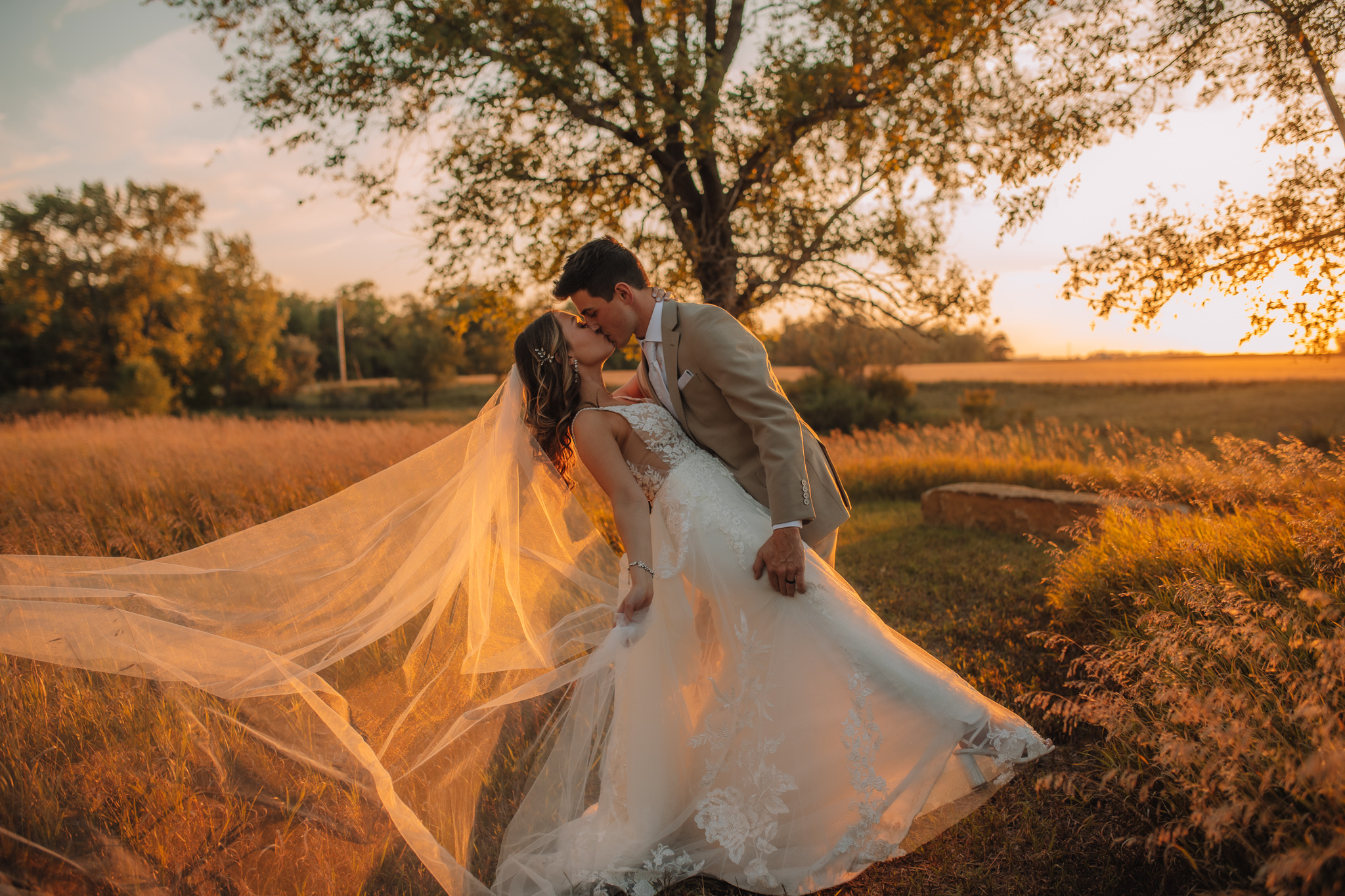 Sunset portrait of Bride and Groom kissing with her veil blowing in the wind