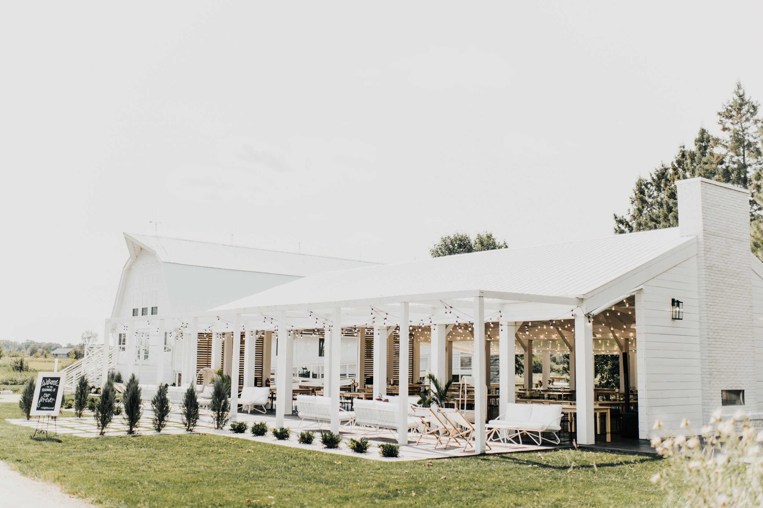 White modern farmhouse-style wedding venue with a covered patio and large windows, set in a lush, green landscape under a clear sky. This venue is called Ivory North