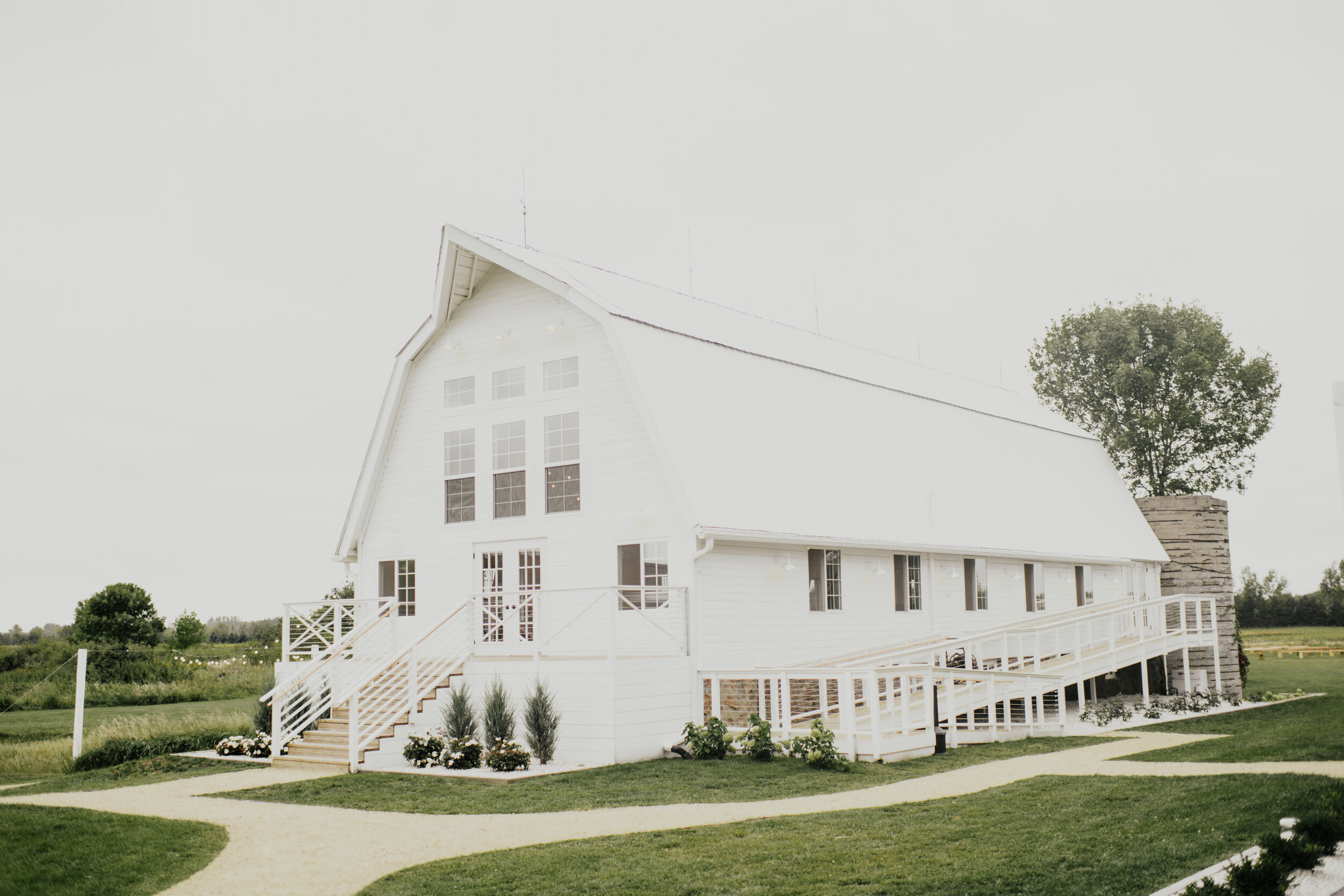 White modern farmhouse-style venue with a covered patio and large windows, set in a lush, green landscape under a clear sky at a wedding in Minnesota