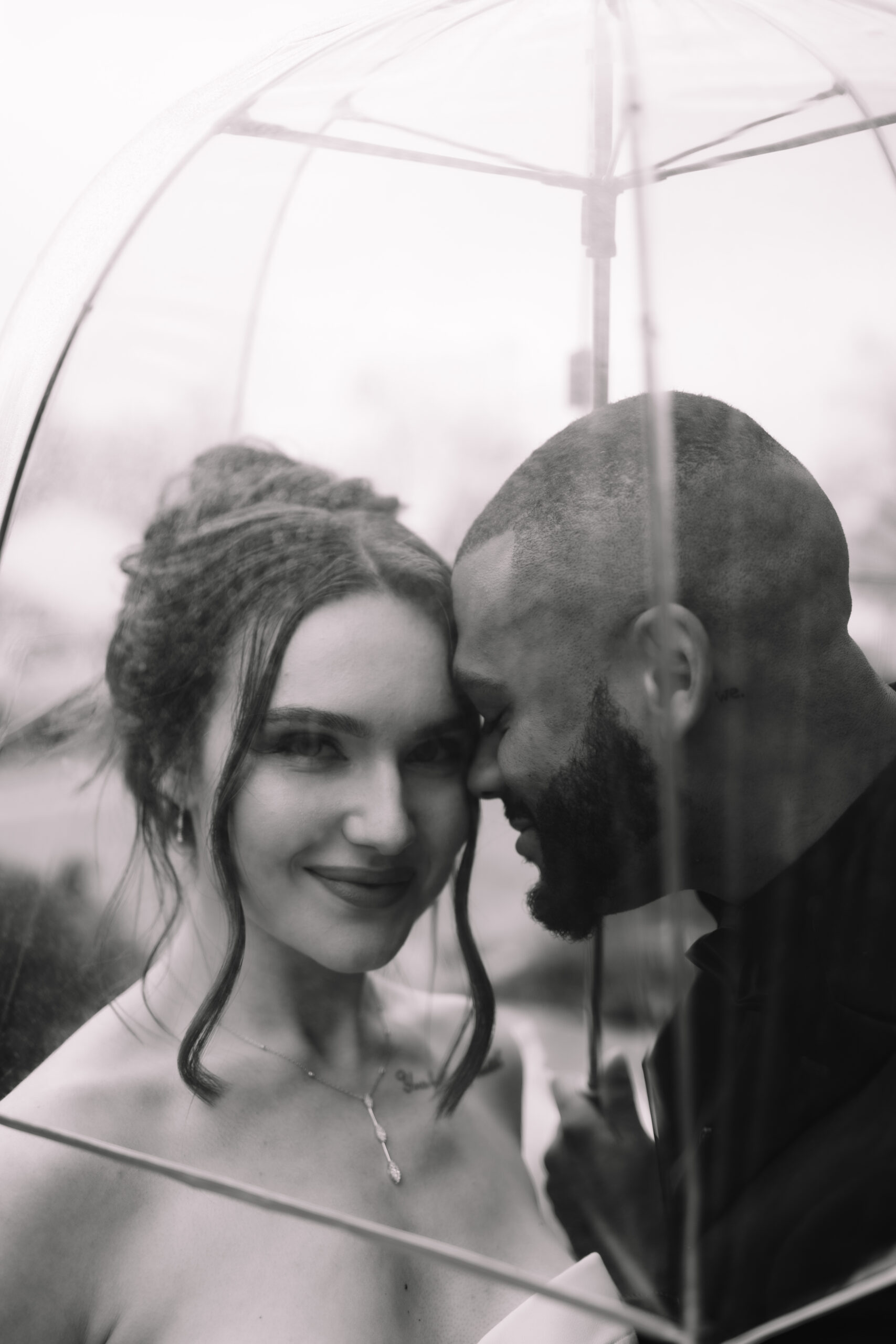 Close up wedding shot of Bride and groom standing underneath a clear umbrella with small rain droplets on, at the Machine Shop Wedding venue in Minneapolis