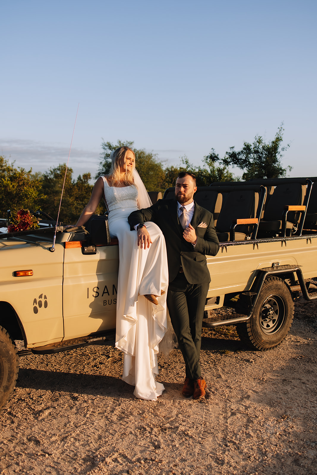 A bride in a white gown and veil on a safari elopement in south africa.They are outdoors with trees and sky in the background.