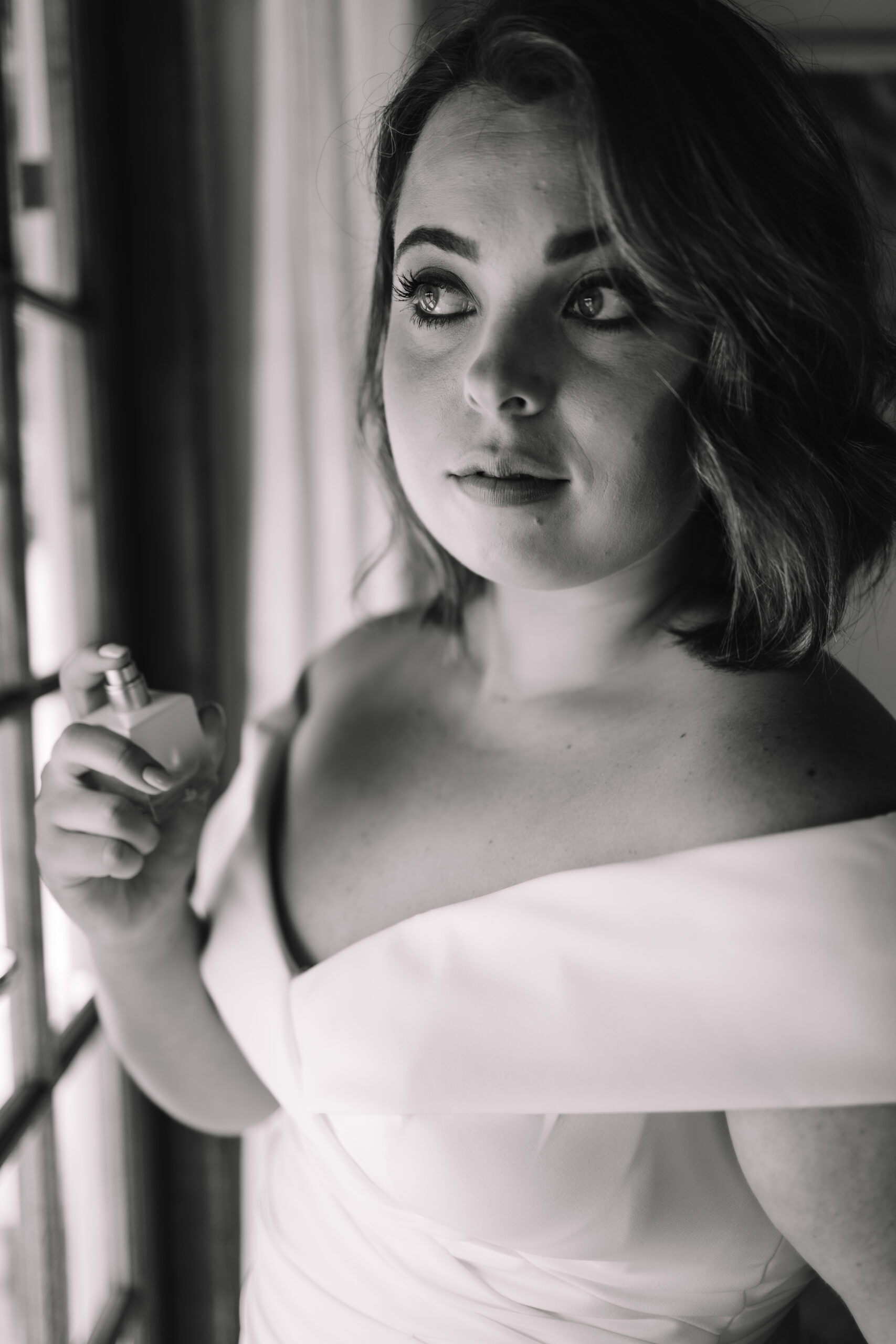 Black and white close up portrait of bride spraying perfume on her neck