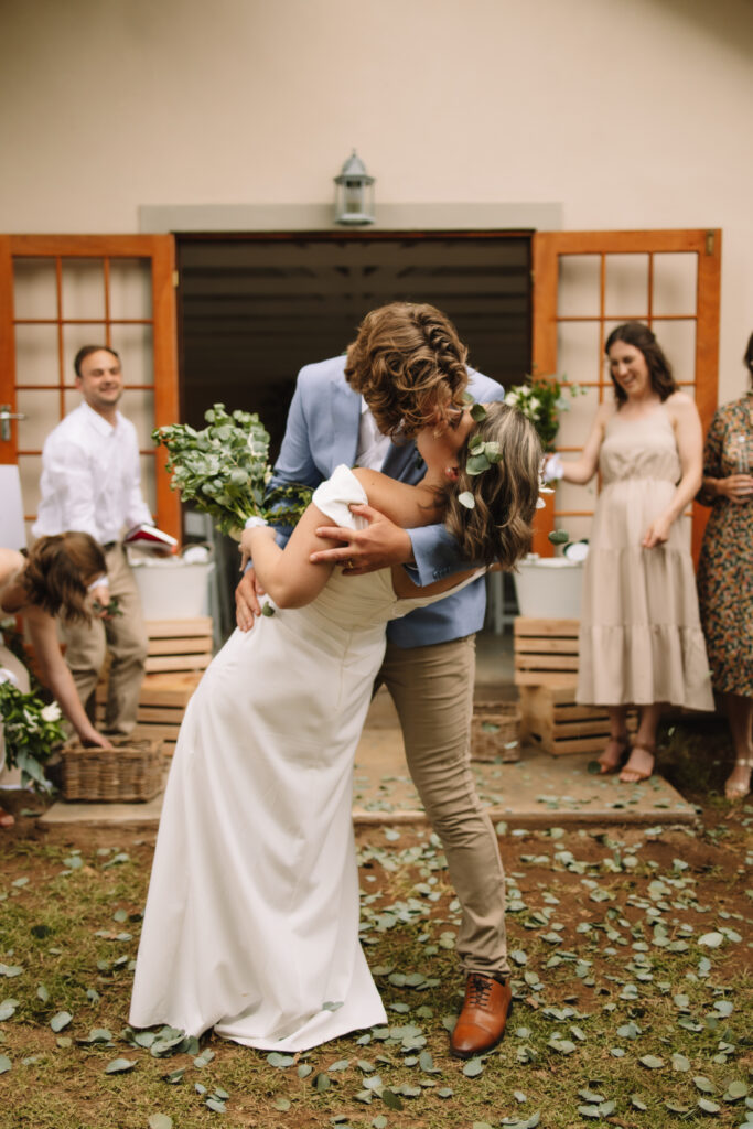 Bride and Groom dip kissing while guests throw eucalyptus confetti at them