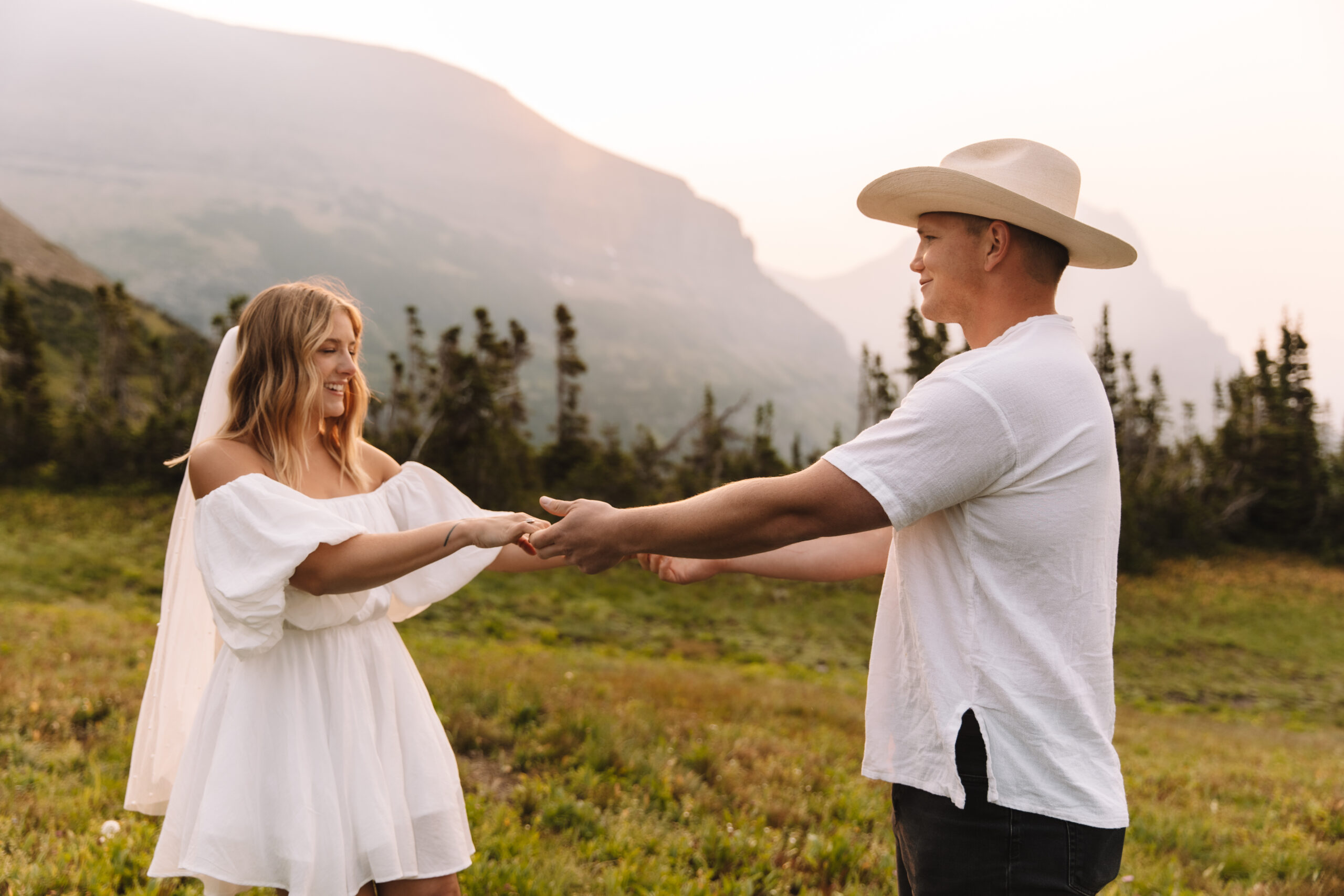 Groom seeing his bride for the first time, taking her hand and smiling at her in her short, flowing, white dress with mountains in the background