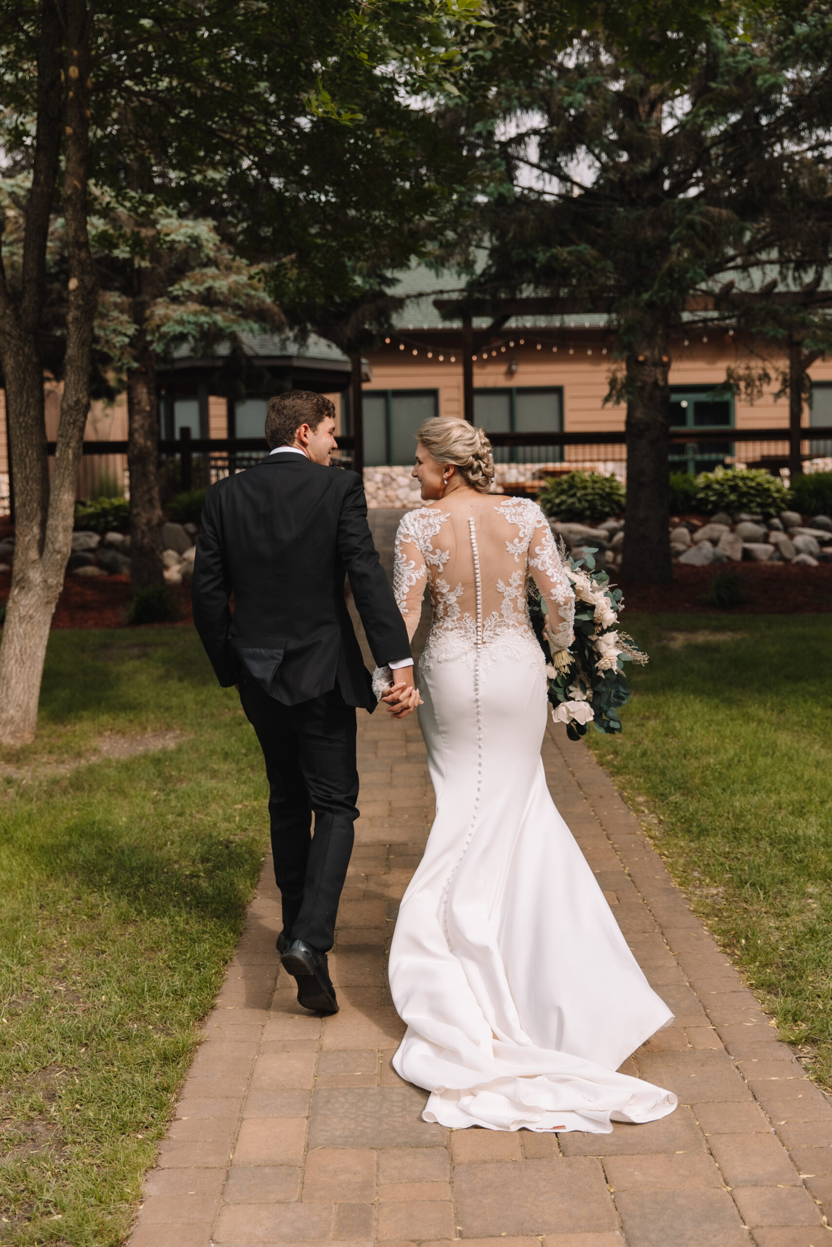 Bride with an open back illusion lace wedding dress with buttons all the way down her spine, walking with her Groom laughing together