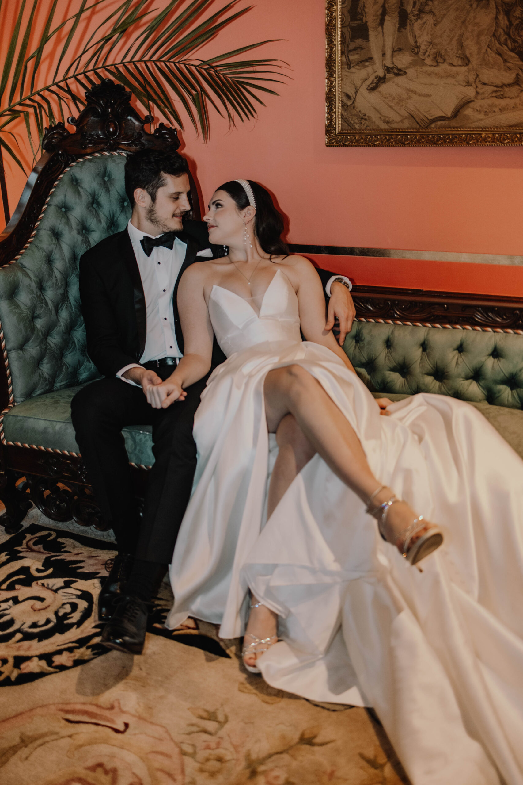 A luxury bride and groom sitting, leaning against each other on a vintage, velvet green couch inside the Van Dusen Mansion in Minneapolis