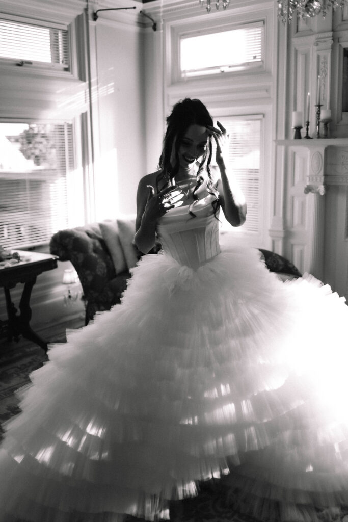 A bride in a voluptuous wedding dress standing in the bridal suite of the van dusen mansion as the sunlight pours through the windows