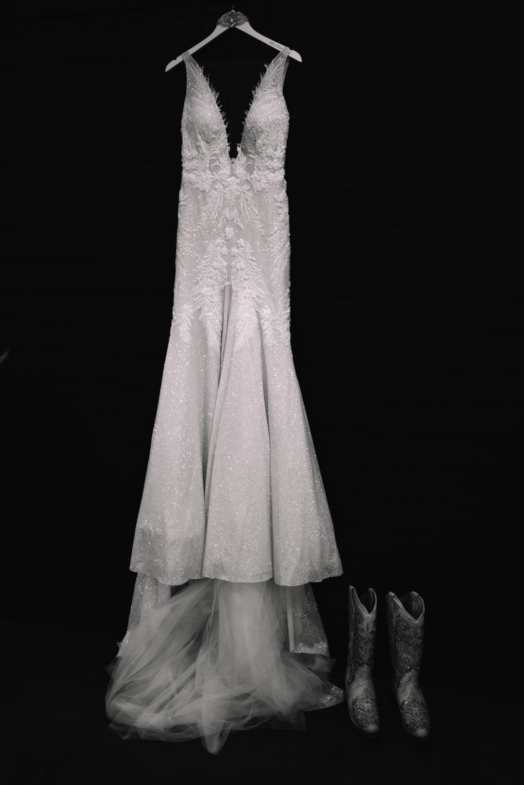 Wedding shot of a sparkly wedding dress with embroidery and lace hanging from a bridal hanger against a black back drop