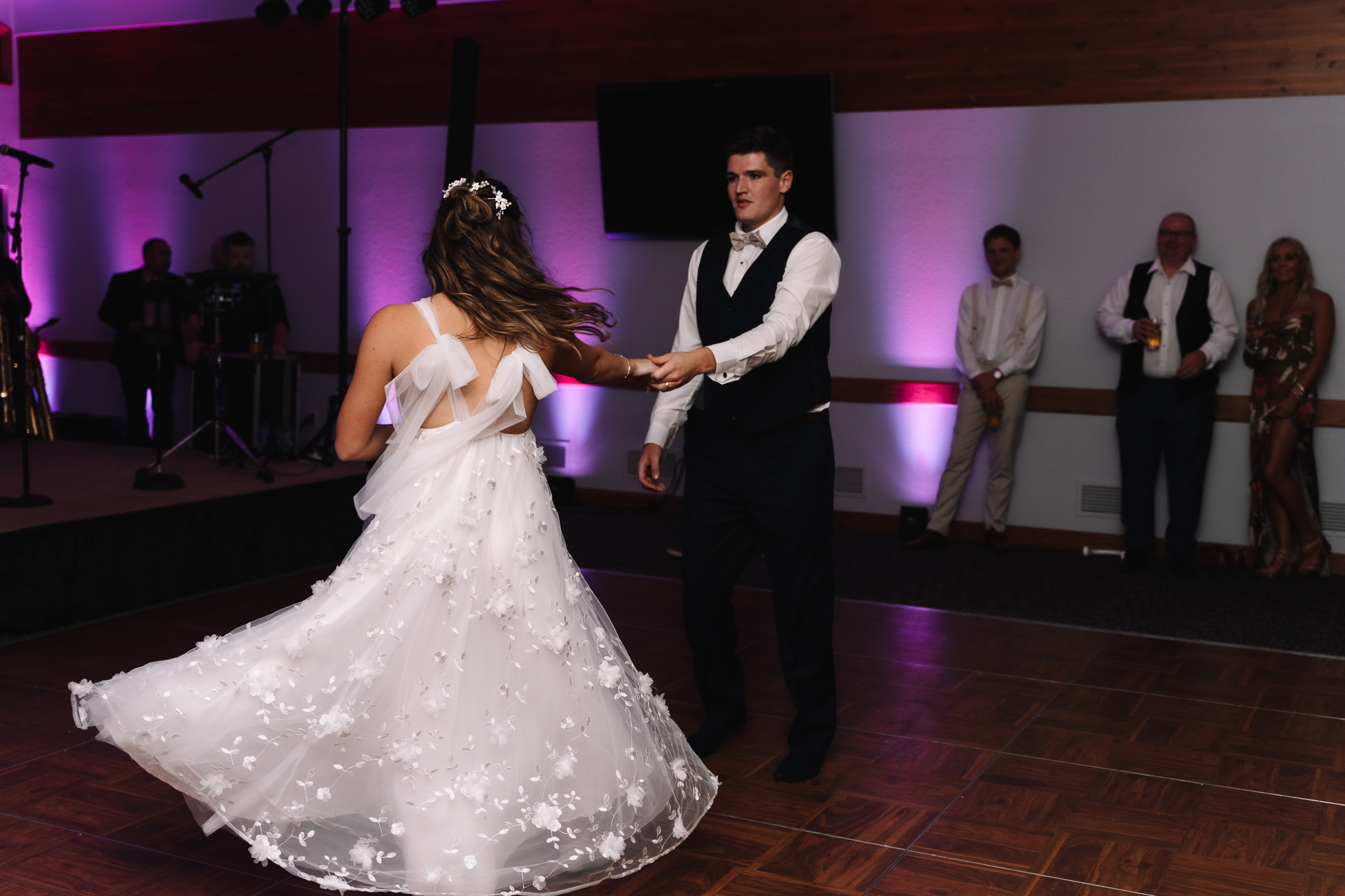 A groom dancing with his bride as her dress twirls and spins around. Purple and pink lights surround the dance floor