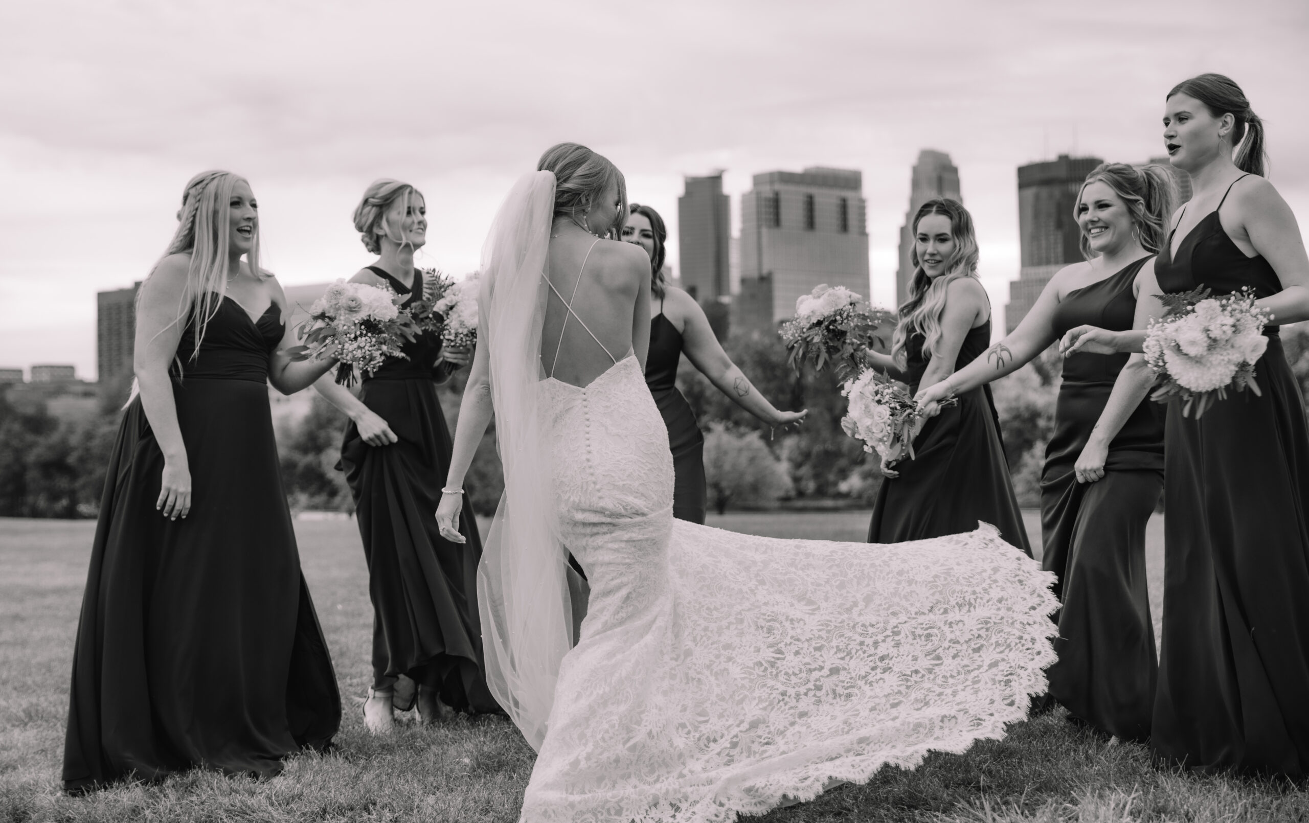 Stunning bride with an open back wedding dress dancing with her bridesmaids in front of the Minneapolis skyline at Boom island park