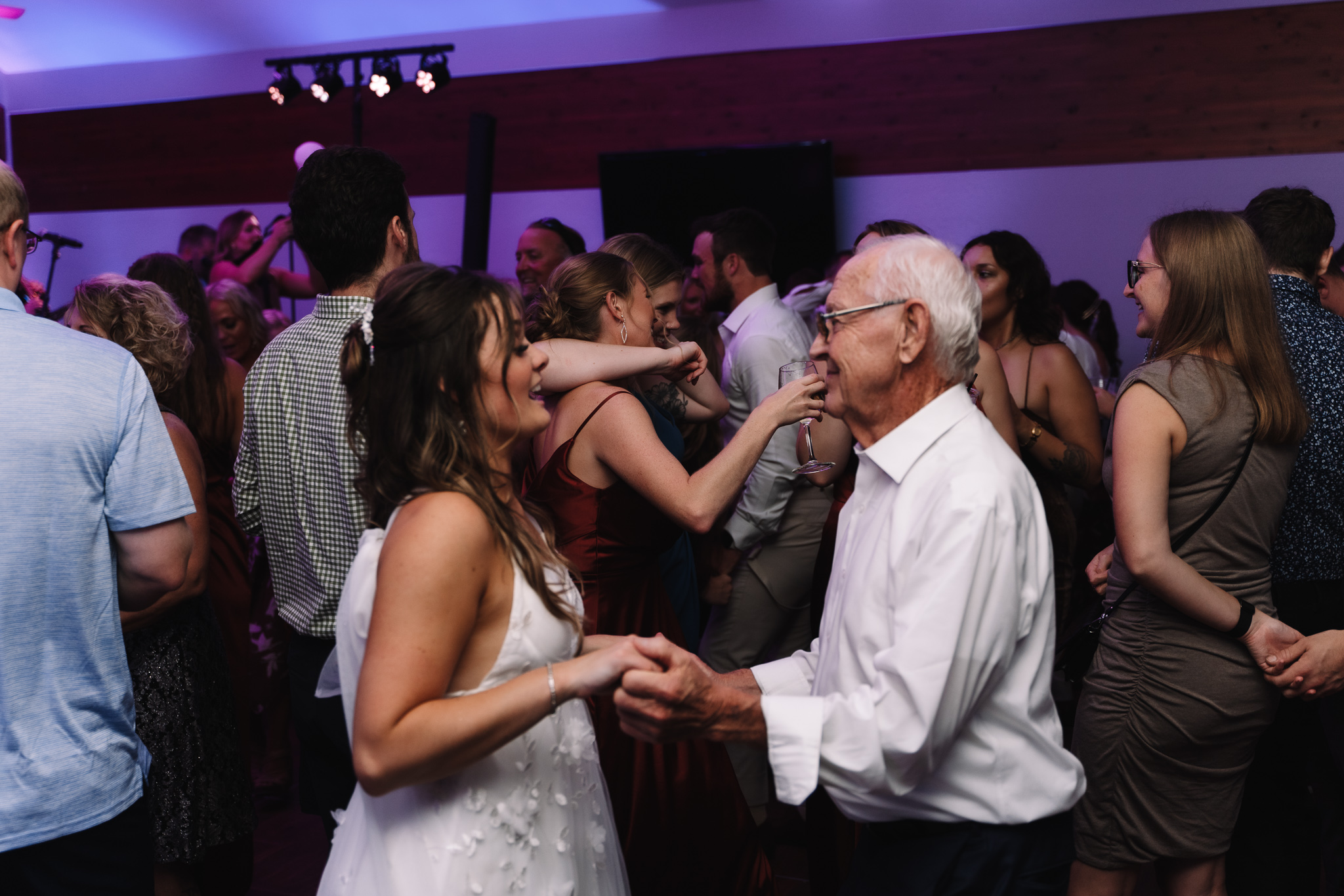 Bride dancing with her grandpa dancing energetically with each other on a dance floor at a lively evening event, with other guests and a live band in the background at a wedding in Minnesota