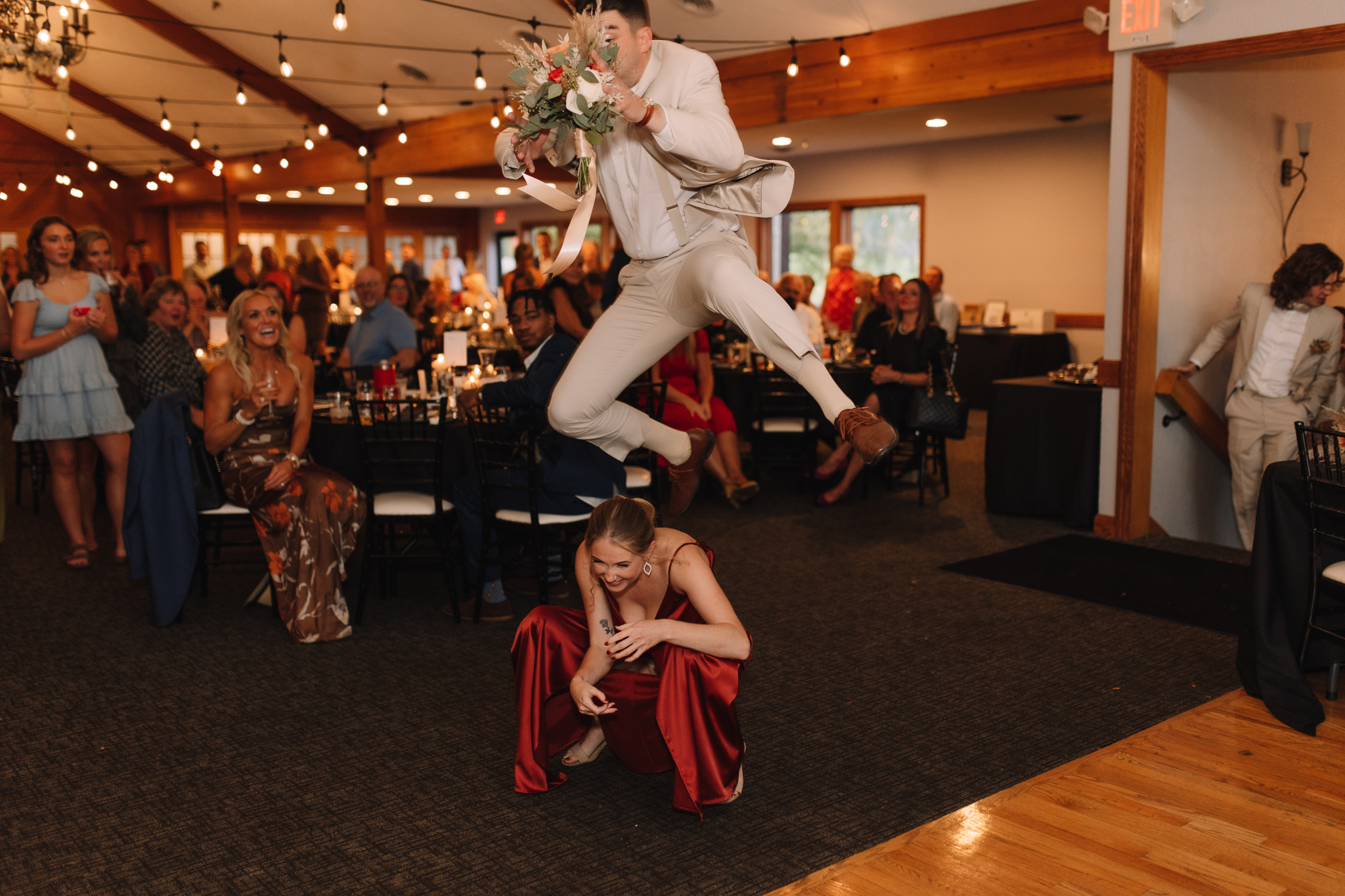 A groomsmen in a light grey suit running and jumping over a bridesmaid who is crouched down for their grand entrance moment
