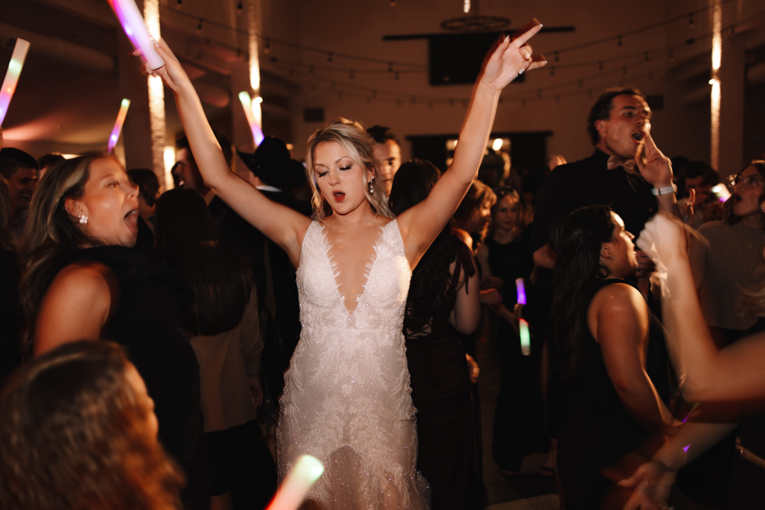 A bride dancing energetically throwing her hands in the air holding a glow stick on the dance floor at her wedding in Minnesota
