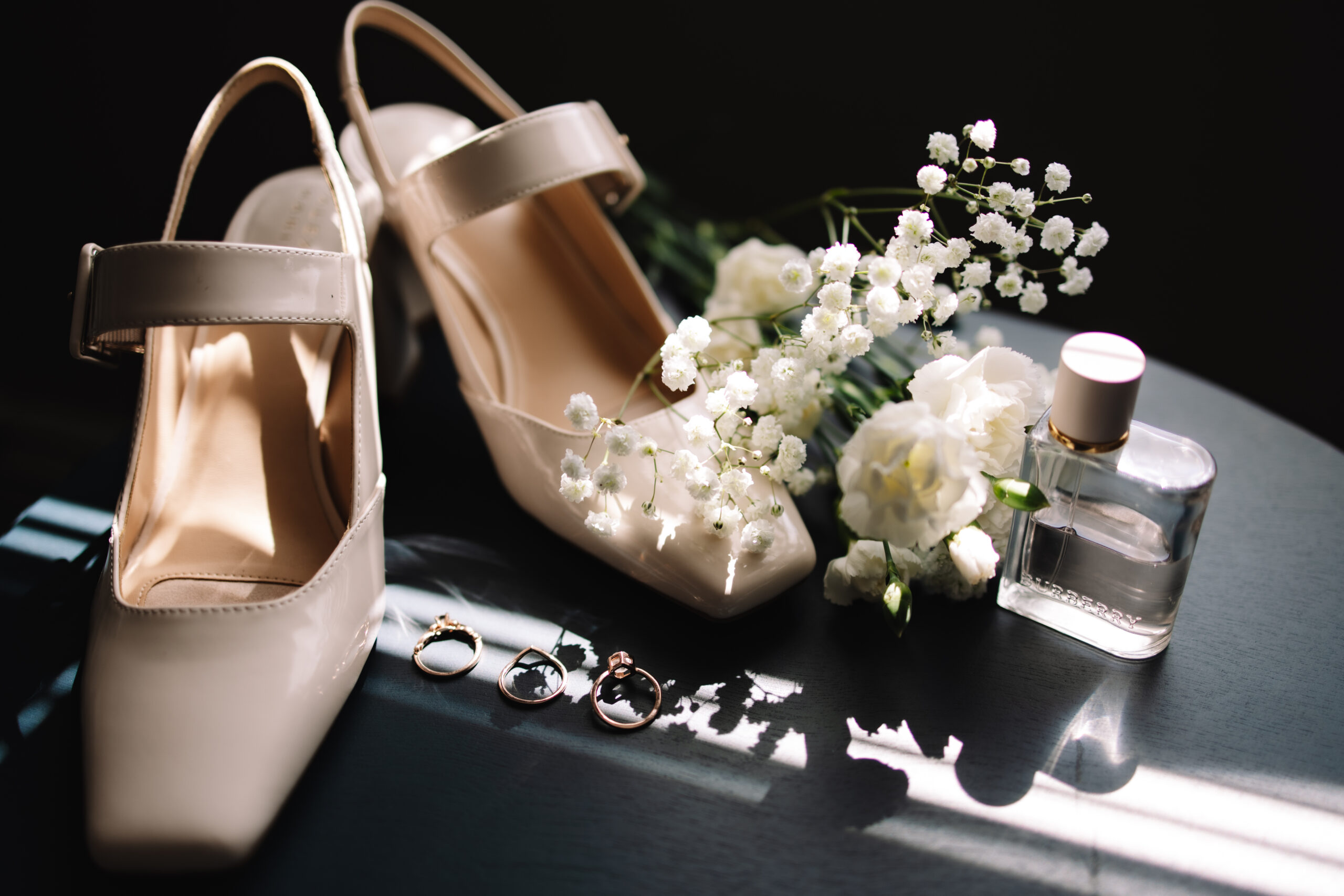 Elegant, simple wedding flat lay detail shot including shoes, white flowers, perfume and rings