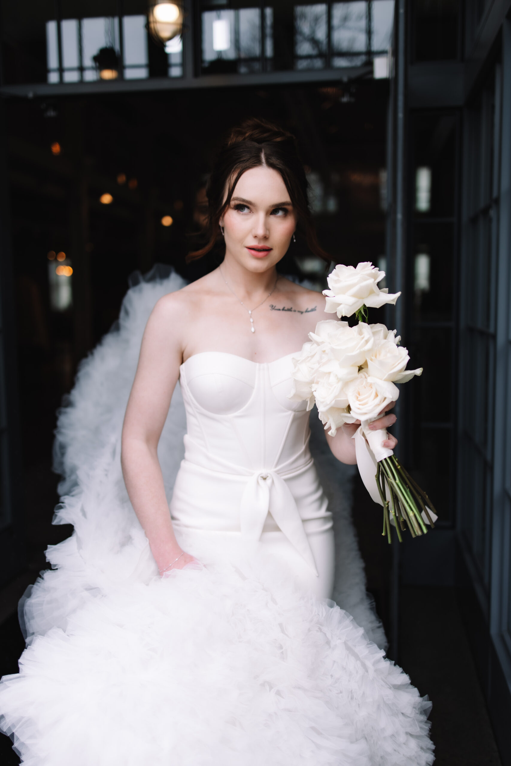 A beautiful modern bride in a voluptuous wedding dress walking out the door holding her white rose bouquet