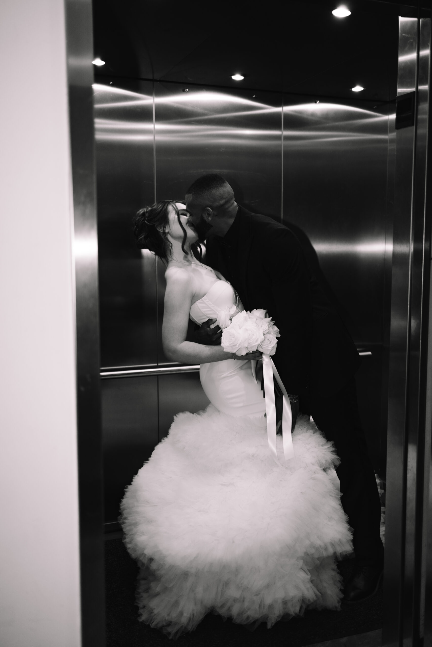 A flash photo of a bride and groom kissing in the elevator as the doors are closing 