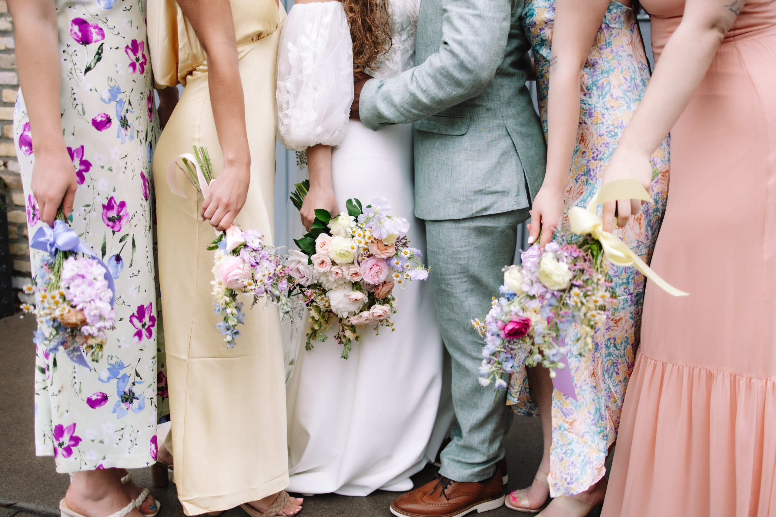 Bridesmaids standing next to the bride in their colorful spring mismatched bridesmaids dresses, holding their colorful spring bouquets next to their sides