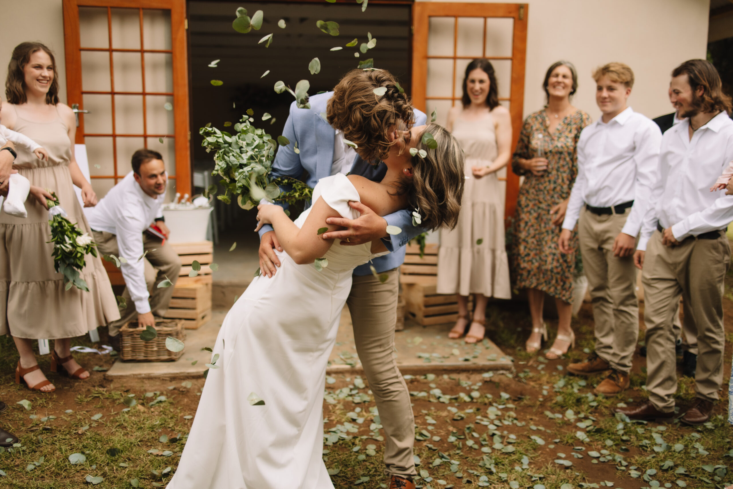 Bride and Groom doing a dip kiss on their way back down the aisle while their guest throw eucalyptus confetti petals towards them