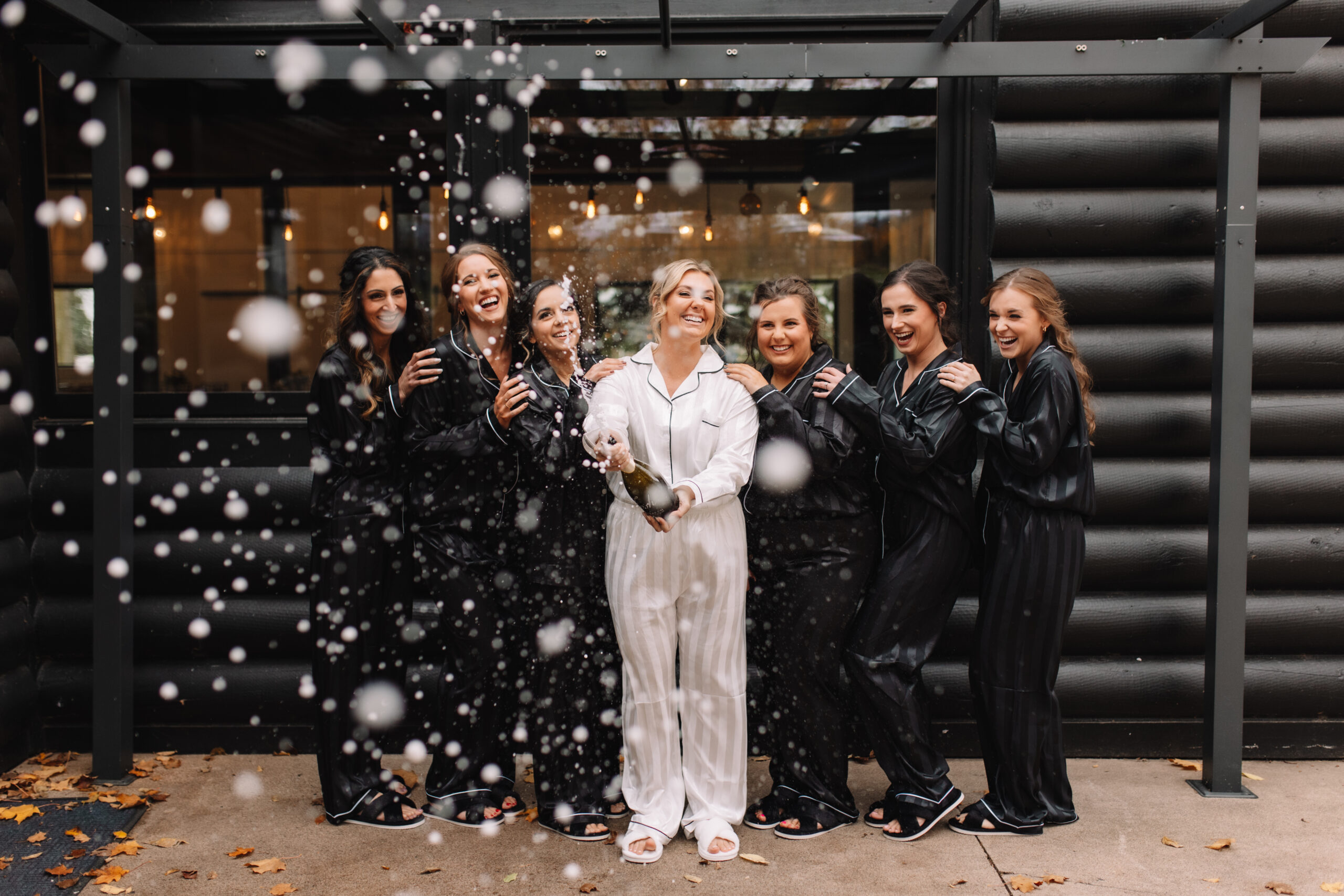 A fun wedding shot of a bride, and her bridesmaids in their matching black outfits, doing a champagne spray to celebrate the start of the wedding day in Minneapolis, Minnesota