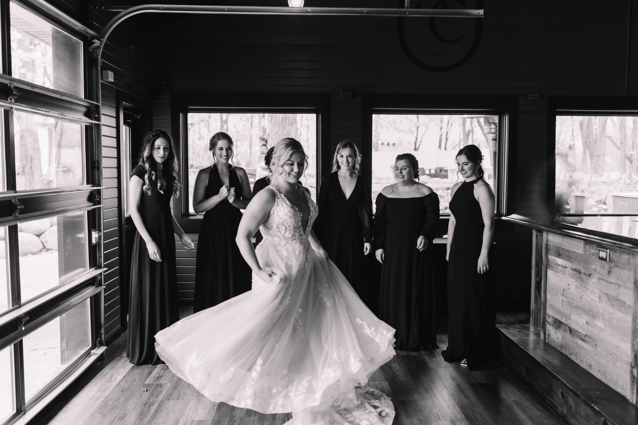 Bride twirling around in her wedding dress revealing her final look to her bridesmaids who are smiling and cheering her on