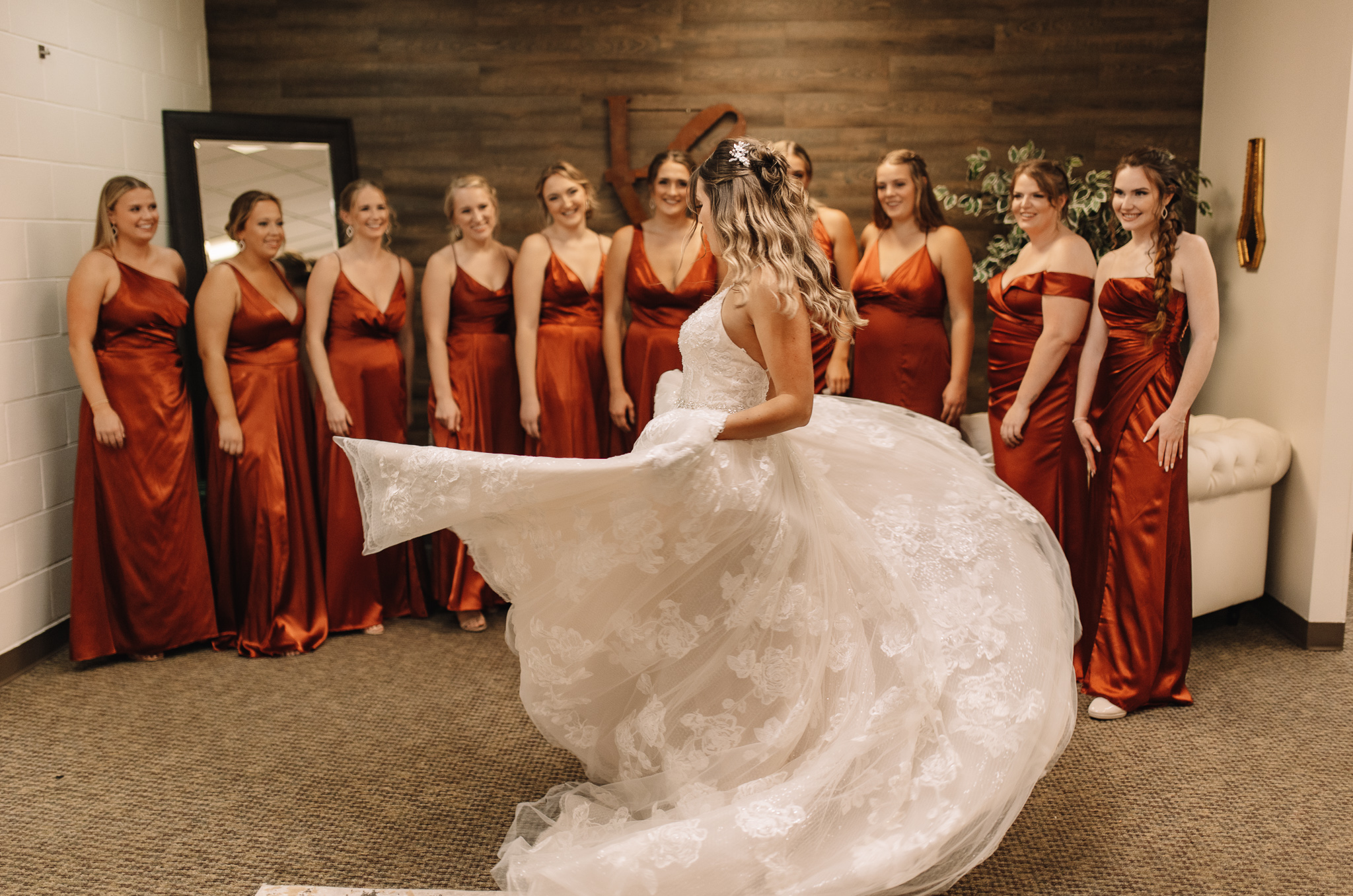 A bride swaying around in her dress in front of her bridesmaids who are wearing terracotta bridesmaids dresses