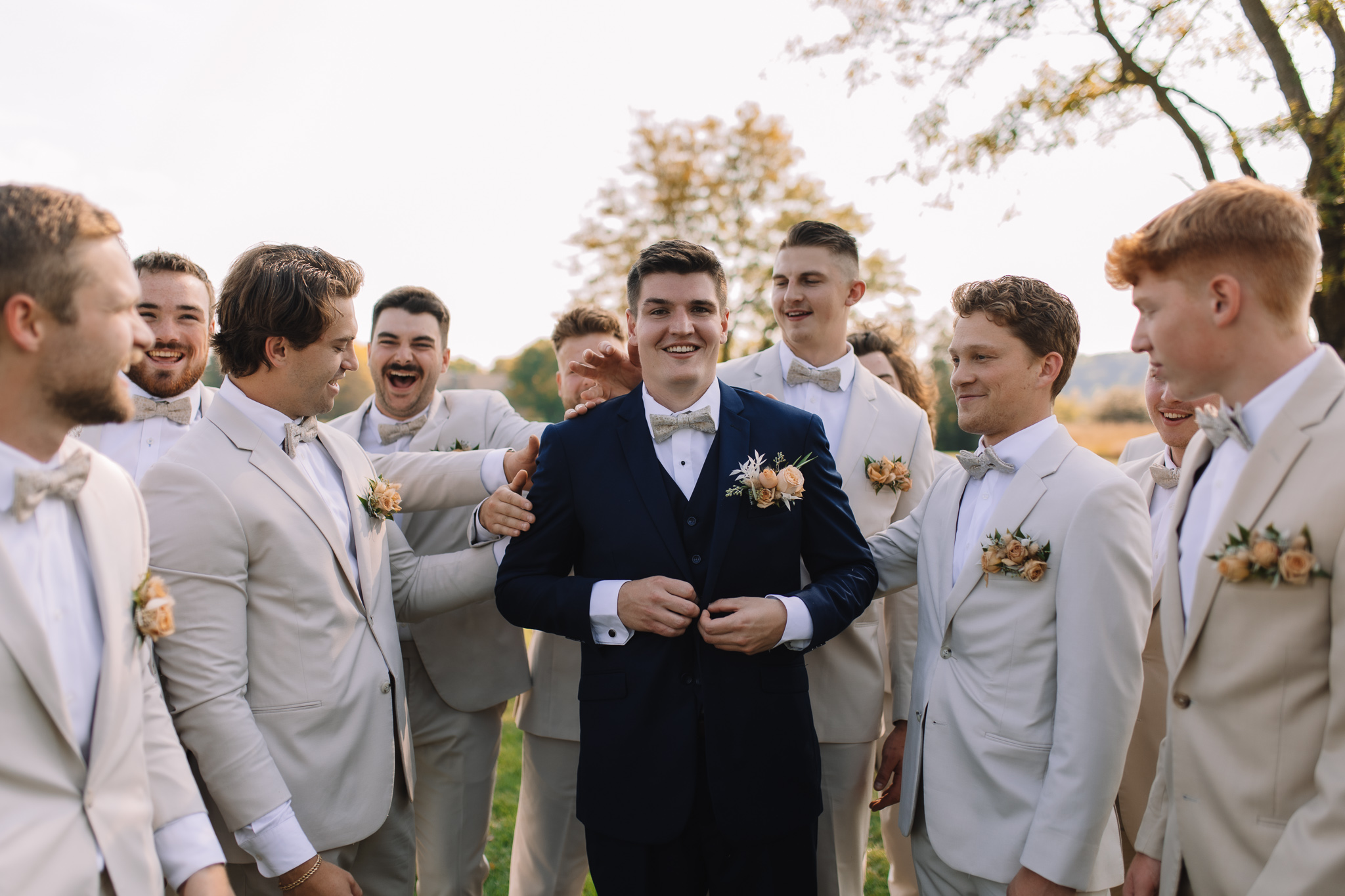 Groom in a navy blue suit surrounded by his groomsmen in oatmeal colored suits with peach boutonniere pocket squares in Stillwater, Minnesota