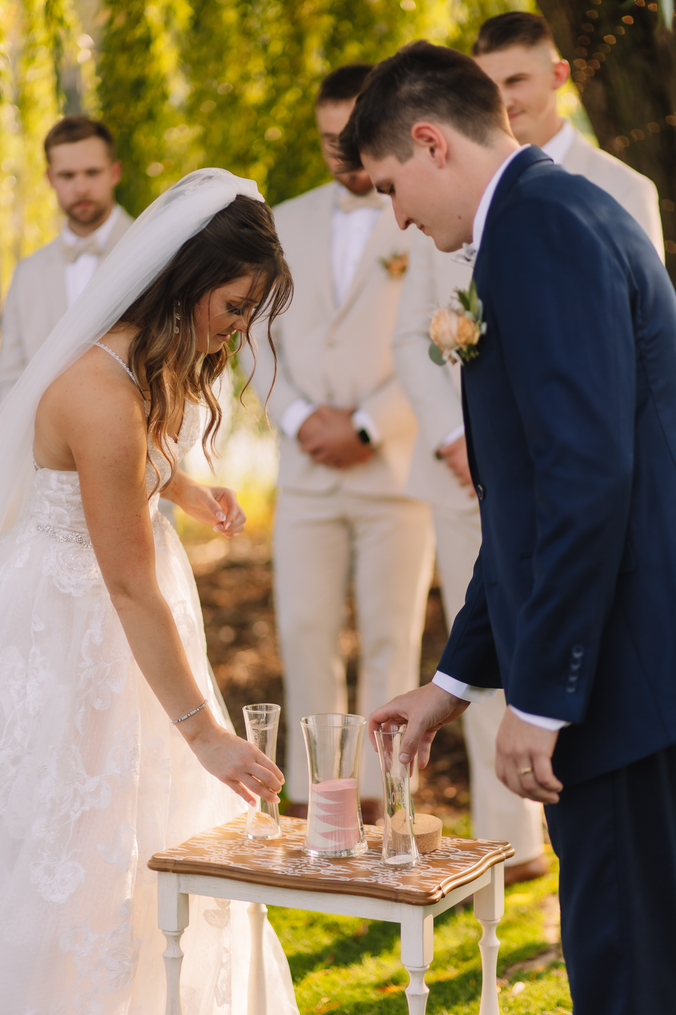 A bride and groom pouring sand together into a glass vase for their outdoor unity ceremony