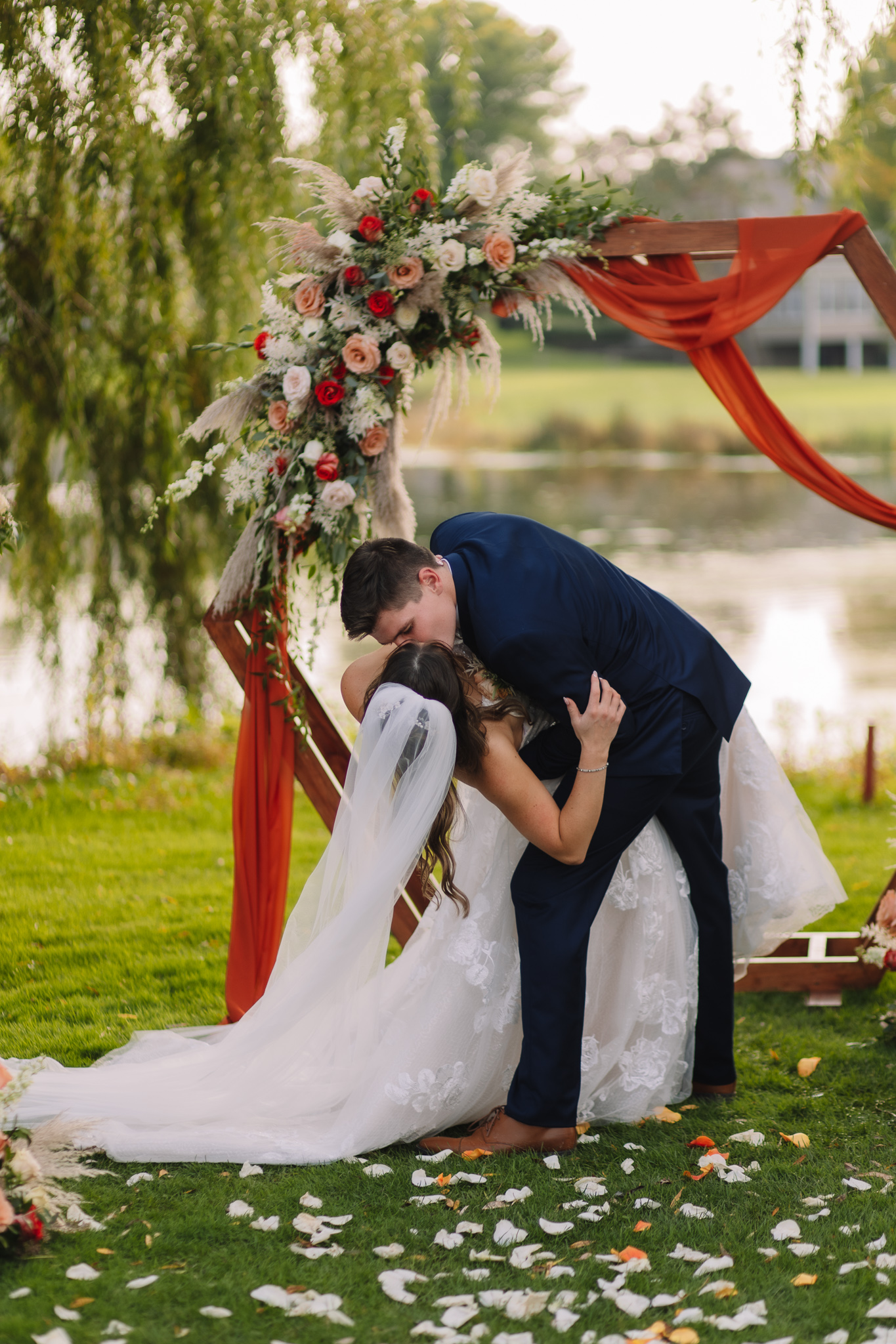 A Groom dipping his Bride and Kissing her in front of the alter, surround by willow trees and a lake.